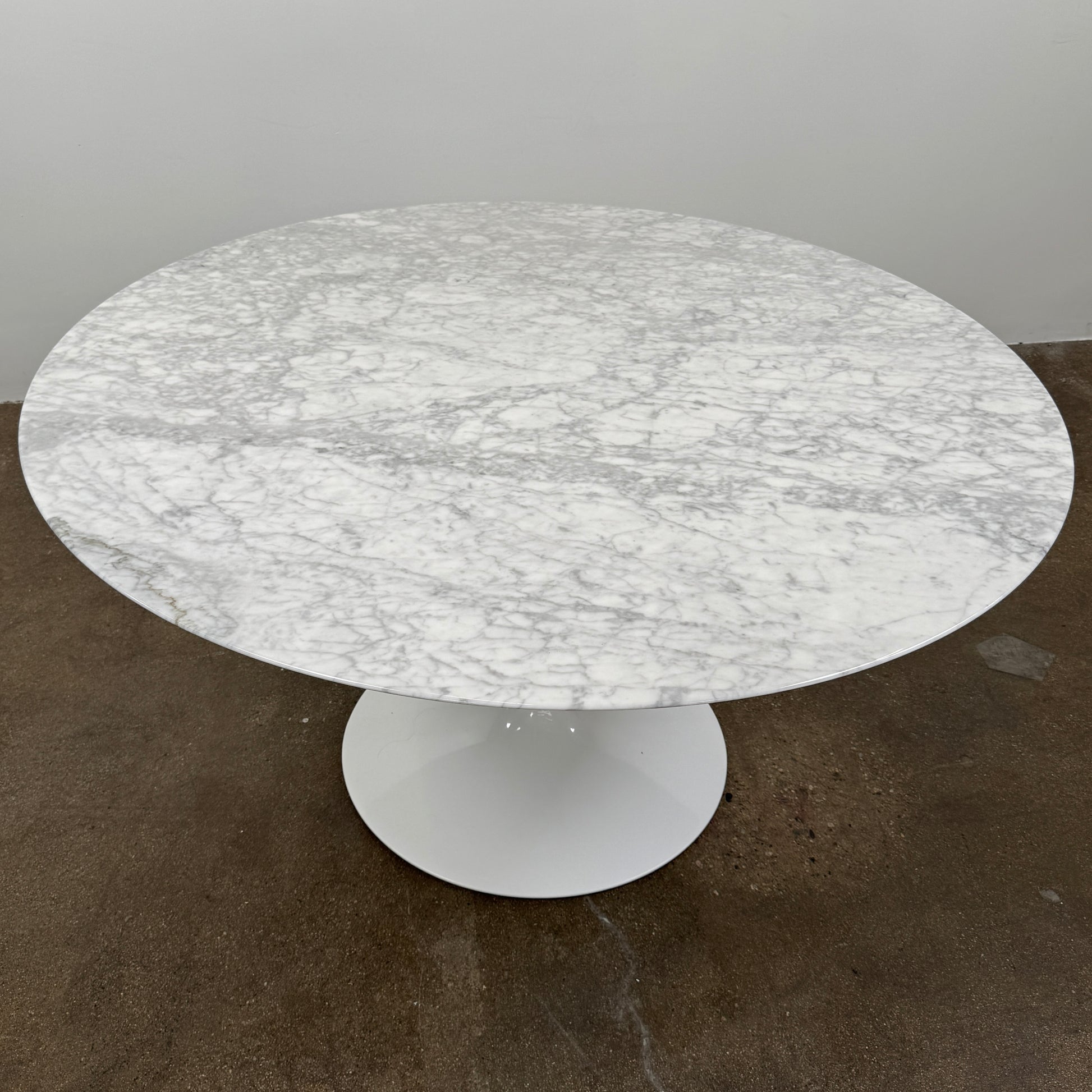 The Knoll Saarinen Table 54″ Round Arabescato Marble, designed by Knoll and inspired by the iconic Saarinen silhouette, features a single central pedestal base and is crafted from luxurious Arabescato marble. It is photographed against a plain white background.