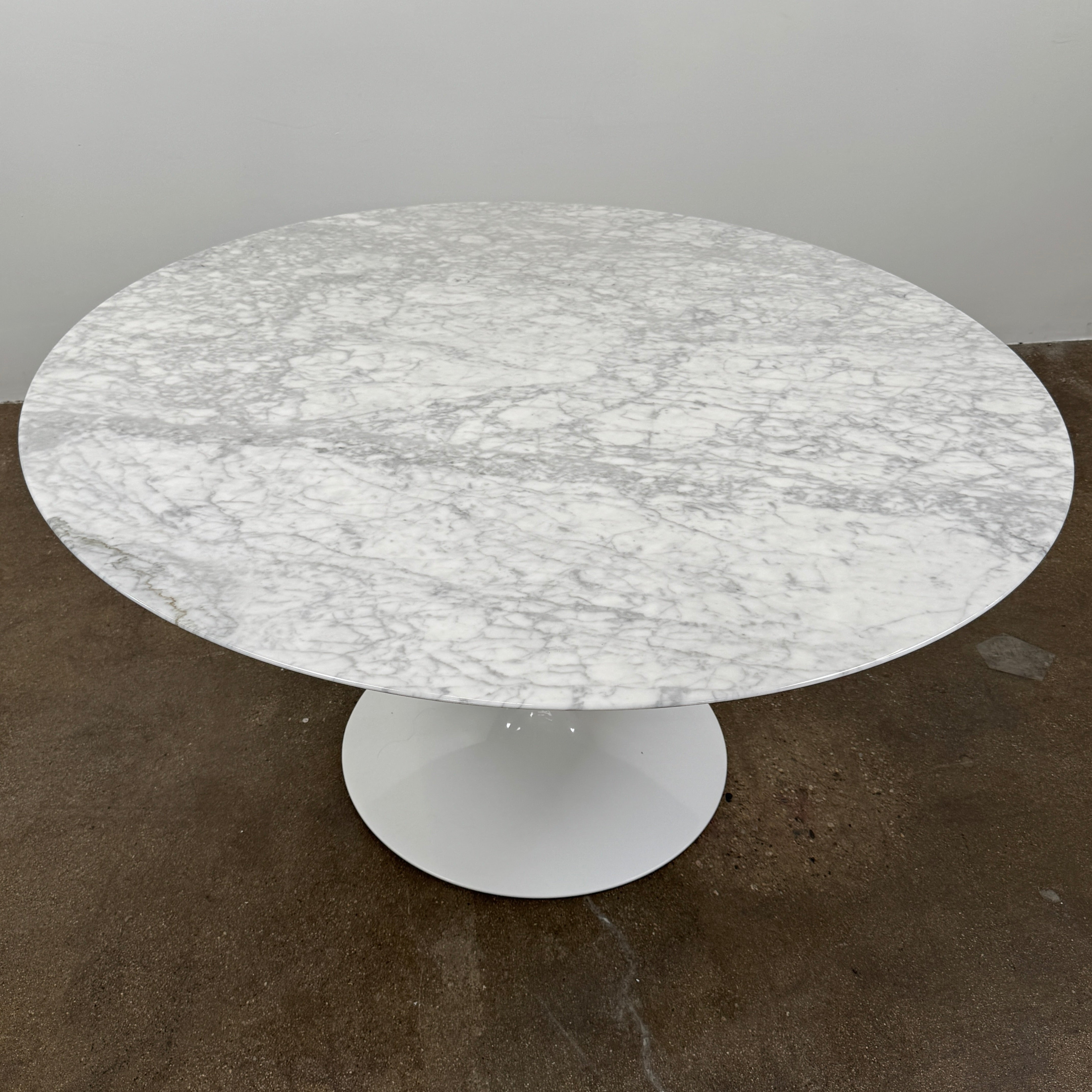 The Knoll Saarinen Table 54″ Round Arabescato Marble, designed by Knoll and inspired by the iconic Saarinen silhouette, features a single central pedestal base and is crafted from luxurious Arabescato marble. It is photographed against a plain white background.