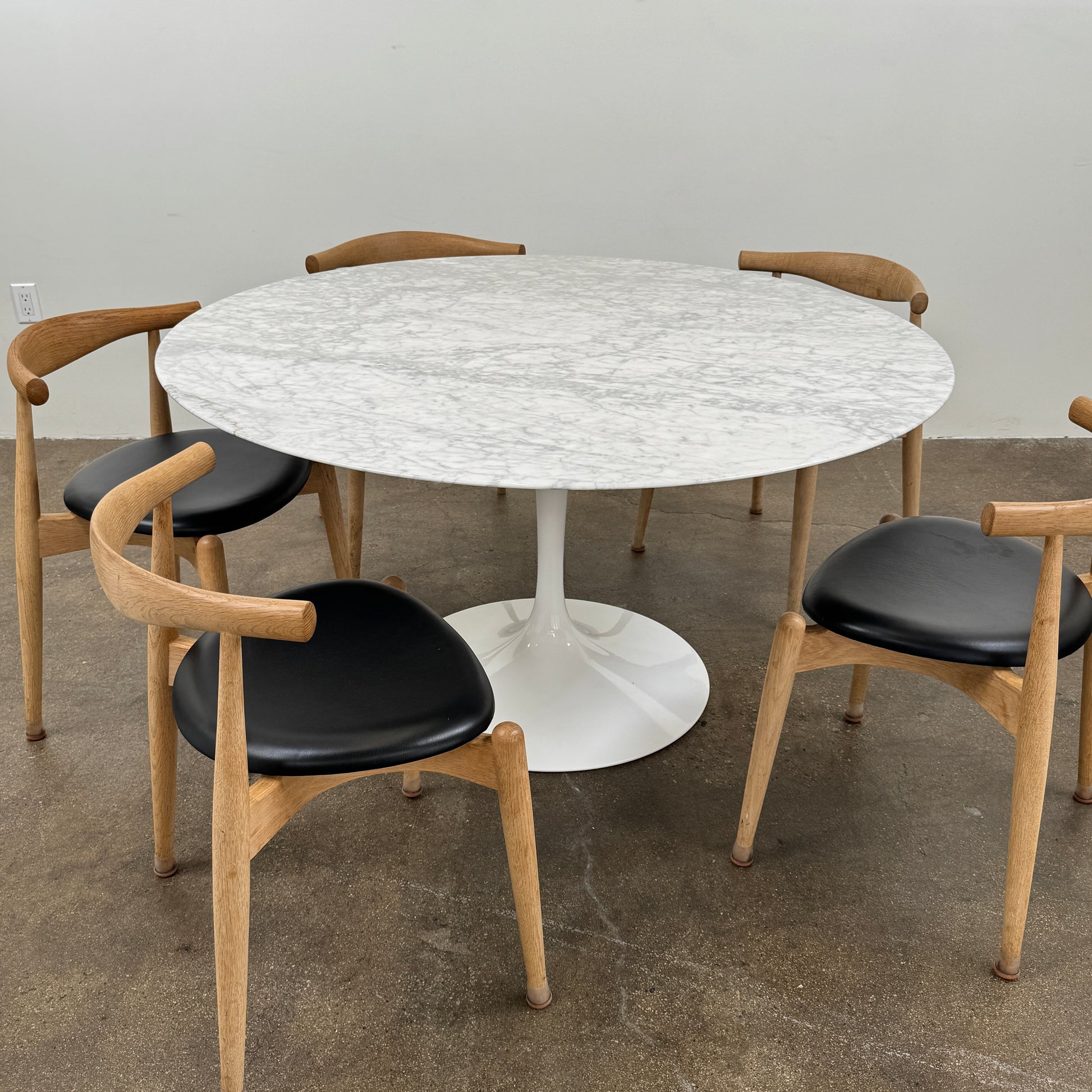 The Knoll Saarinen Table 54″ Round Arabescato Marble, designed by Knoll and inspired by the iconic Saarinen silhouette, features a single central pedestal base and is crafted from luxurious Arabescato marble. It is photographed against a plain white background.