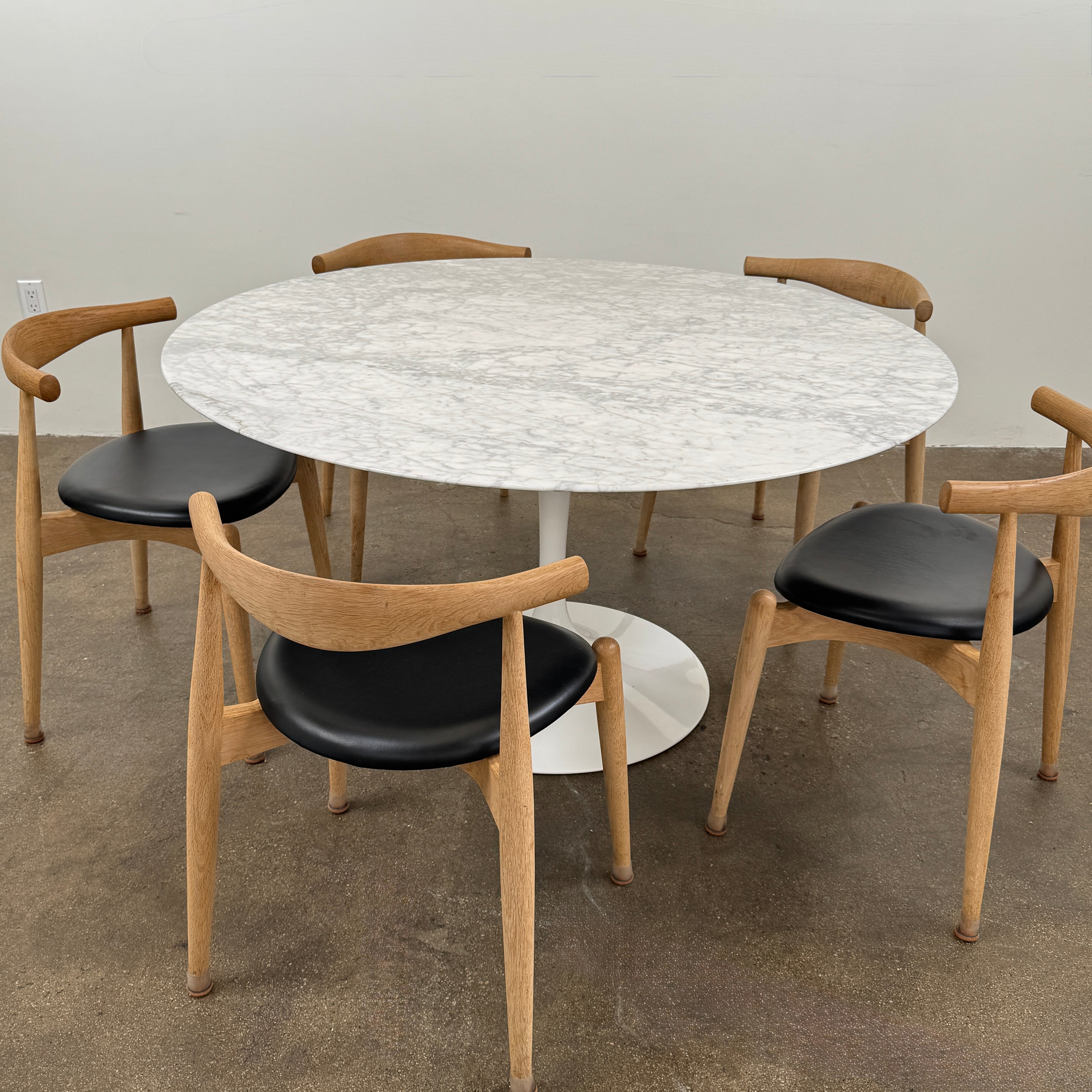 The Knoll Saarinen Table 54″ Round Arabescato Marble, designed by Knoll and inspired by the iconic Saarinen silhouette, features a single central pedestal base and is crafted from luxurious Arabescato marble. It is photographed against a plain white background.