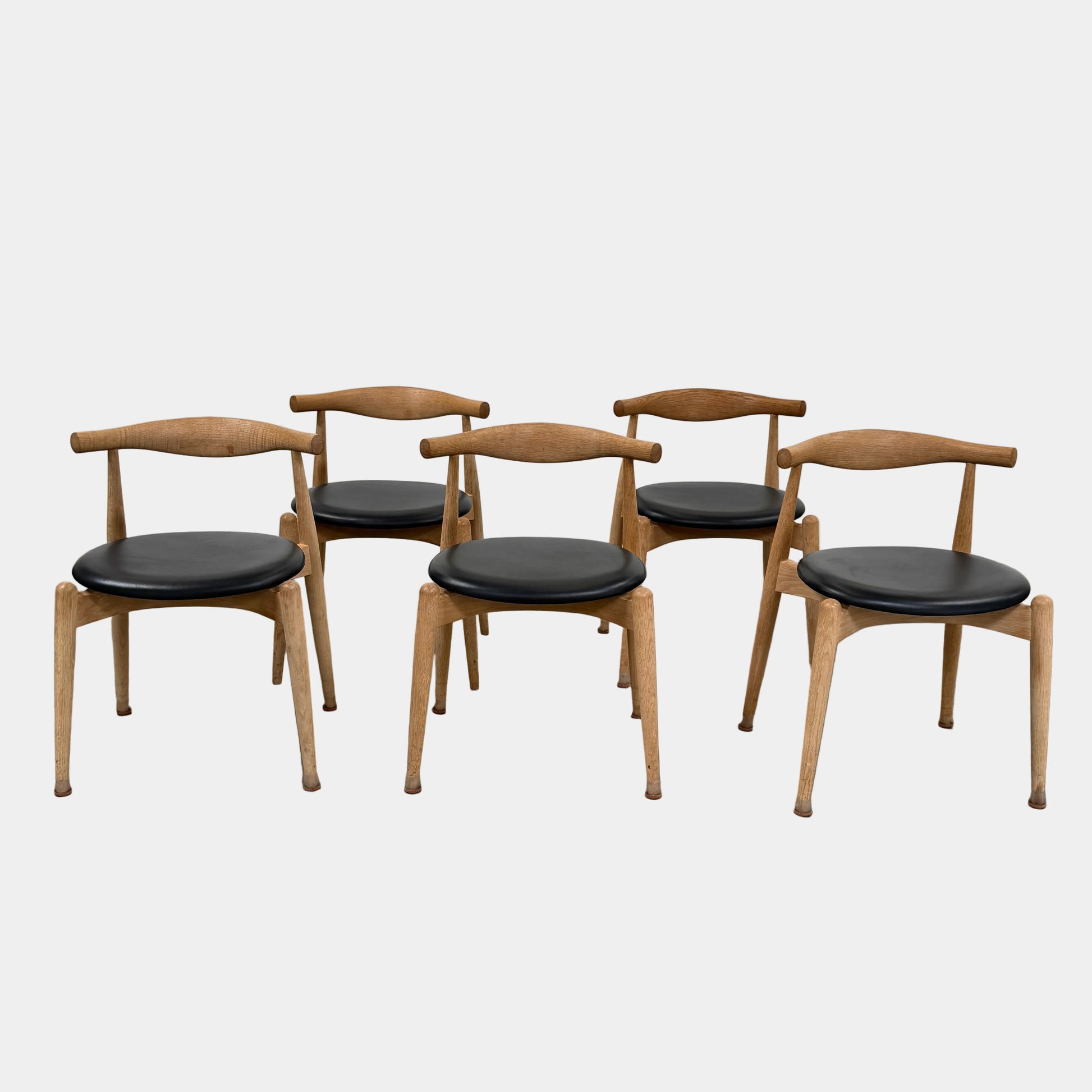 A set of five Carl Hansen & Son CH20 Elbow Chairs by Carl Hansen & Son, each with a curved wooden backrest and a round black seat cushion, are arranged in two rows against a plain white background.