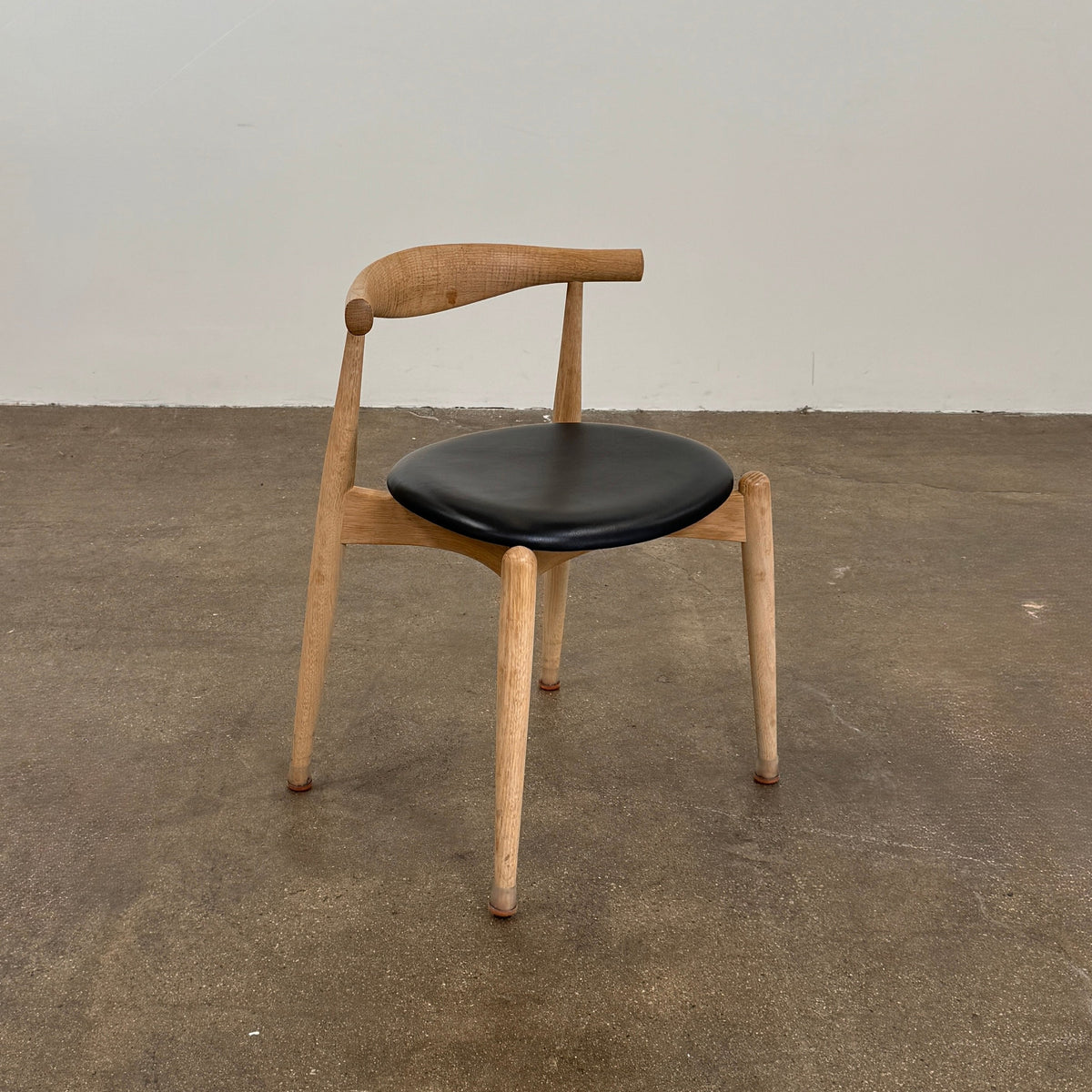 A set of five Carl Hansen & Son CH20 Elbow Chairs by Carl Hansen & Son, each with a curved wooden backrest and a round black seat cushion, are arranged in two rows against a plain white background.