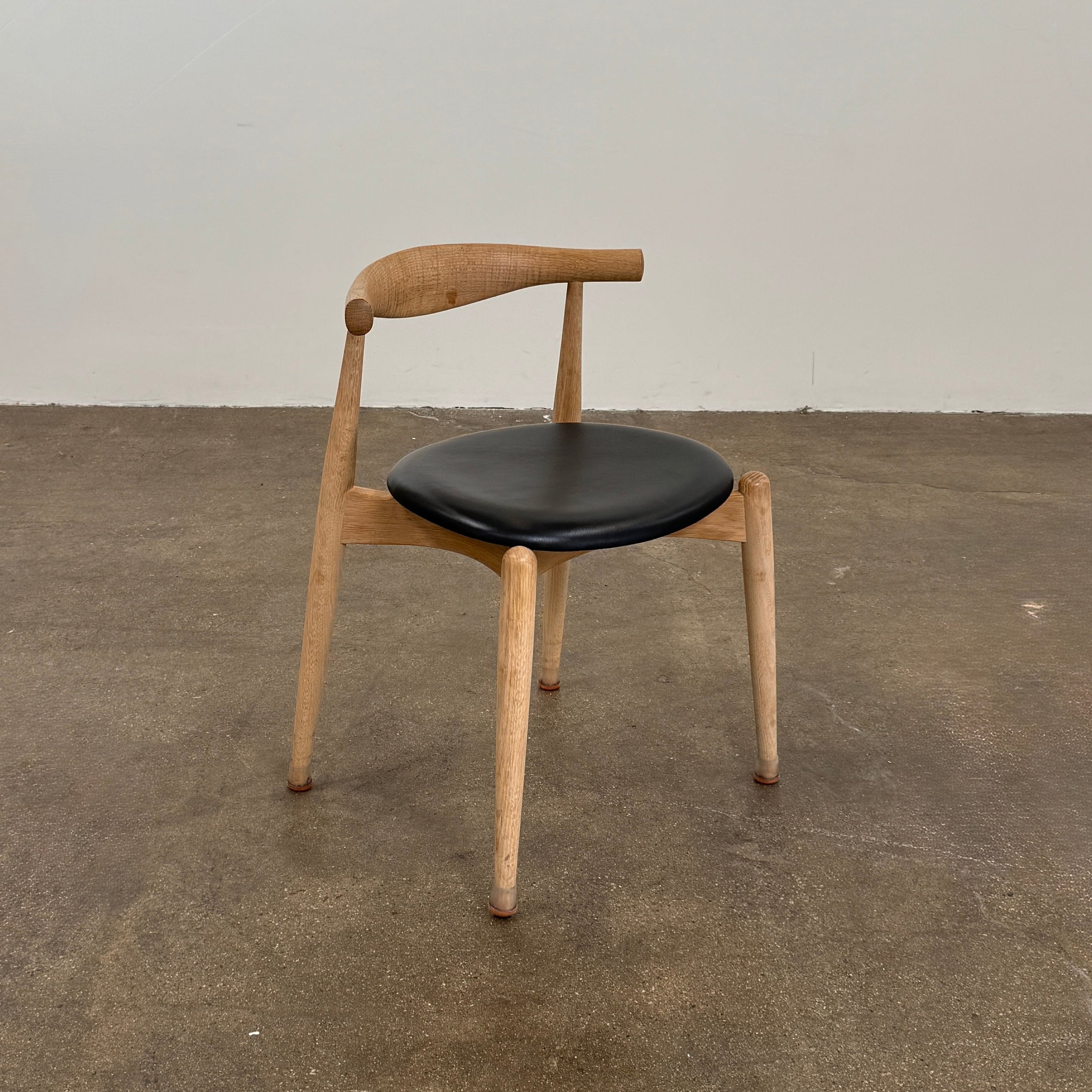 A set of five Carl Hansen & Son CH20 Elbow Chairs by Carl Hansen & Son, each with a curved wooden backrest and a round black seat cushion, are arranged in two rows against a plain white background.