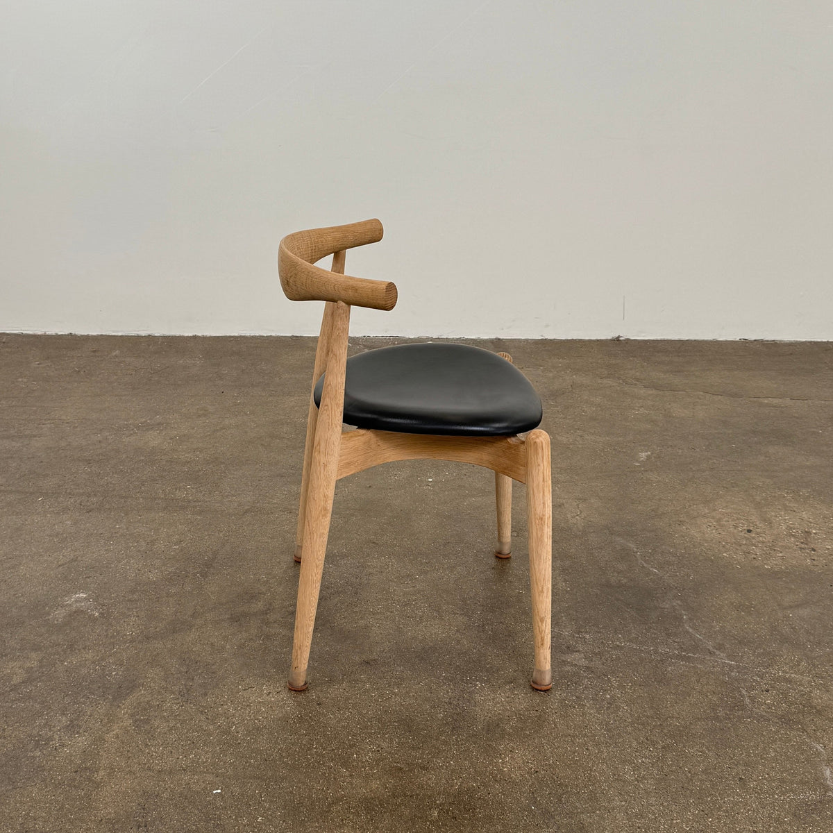 A set of five Carl Hansen & Son CH20 Elbow Chairs by Carl Hansen & Son, each with a curved wooden backrest and a round black seat cushion, are arranged in two rows against a plain white background.