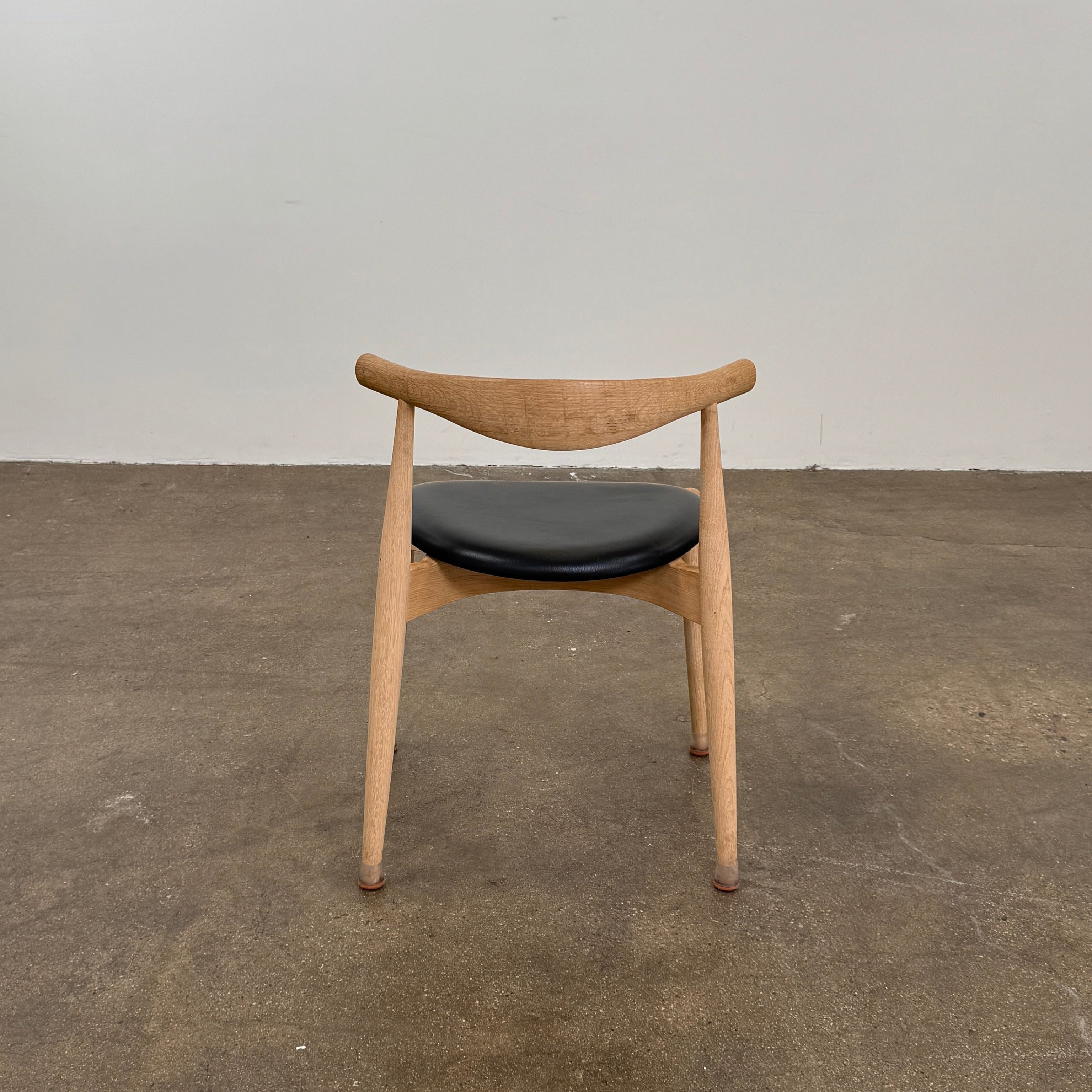A set of five Carl Hansen & Son CH20 Elbow Chairs by Carl Hansen & Son, each with a curved wooden backrest and a round black seat cushion, are arranged in two rows against a plain white background.