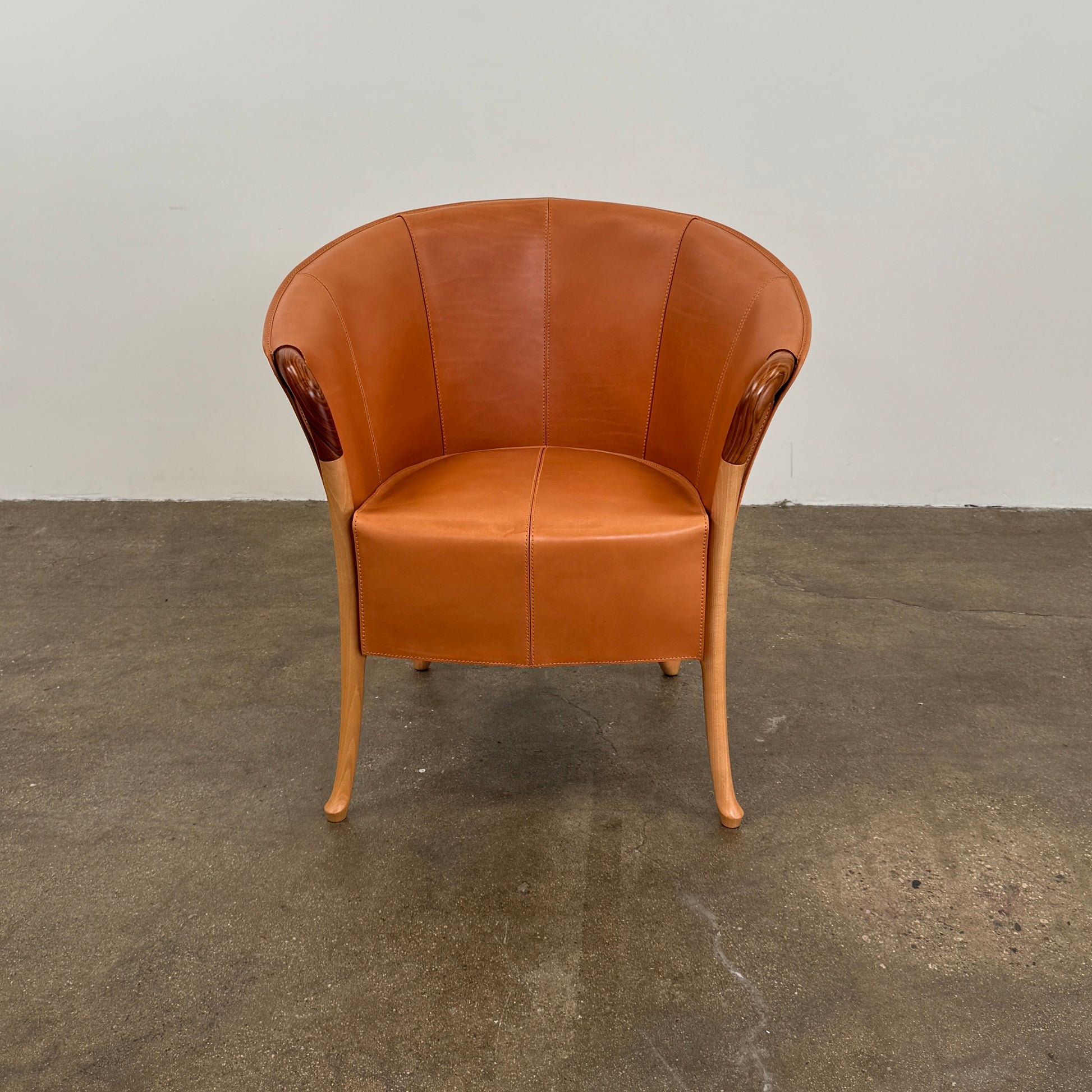 The Giorgetti “Progetti” Armchair by Giorgetti features a brown saddle leather seat, wooden legs, and Pau Ferro armrest accents, presented against a plain white background.