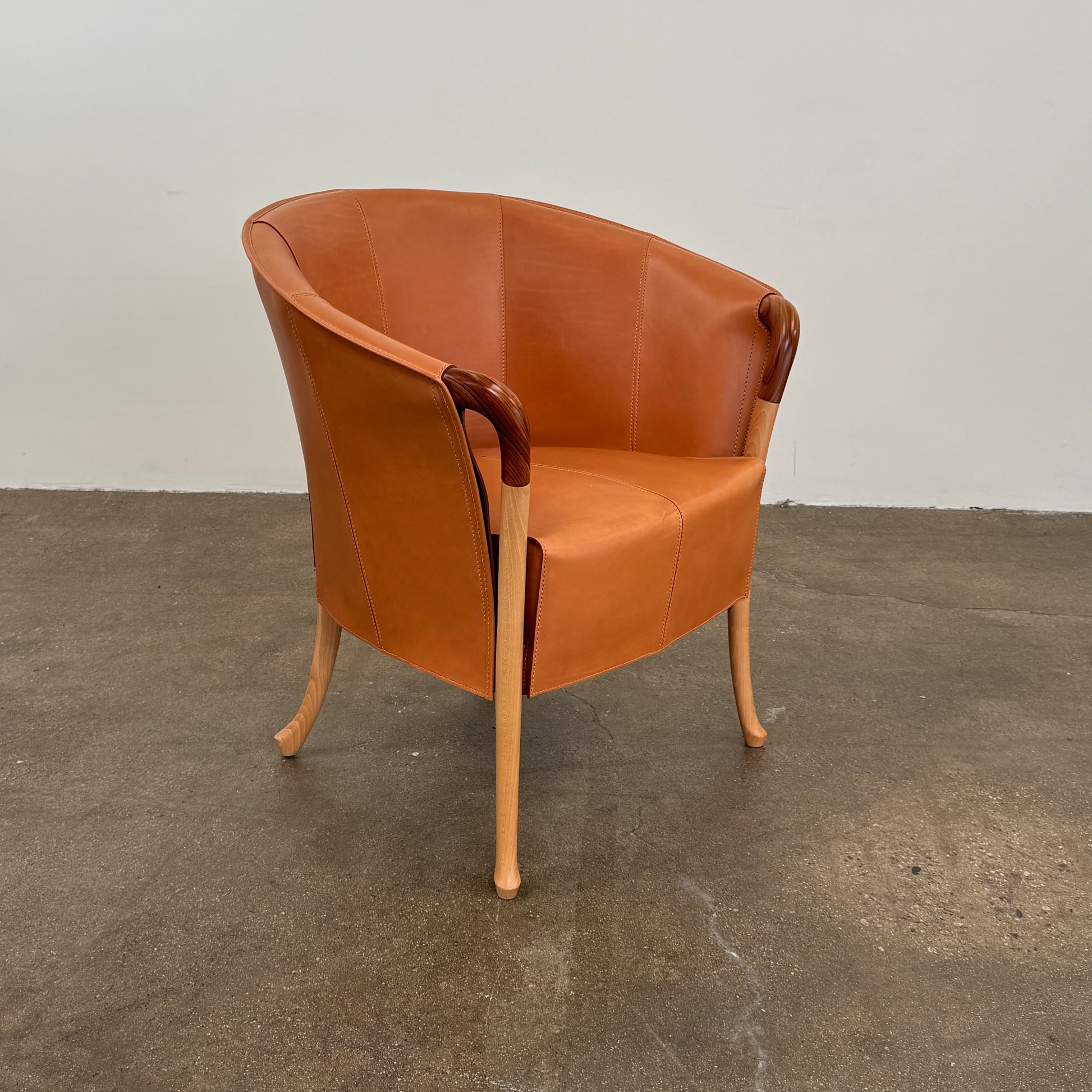 The Giorgetti “Progetti” Armchair by Giorgetti features a brown saddle leather seat, wooden legs, and Pau Ferro armrest accents, presented against a plain white background.