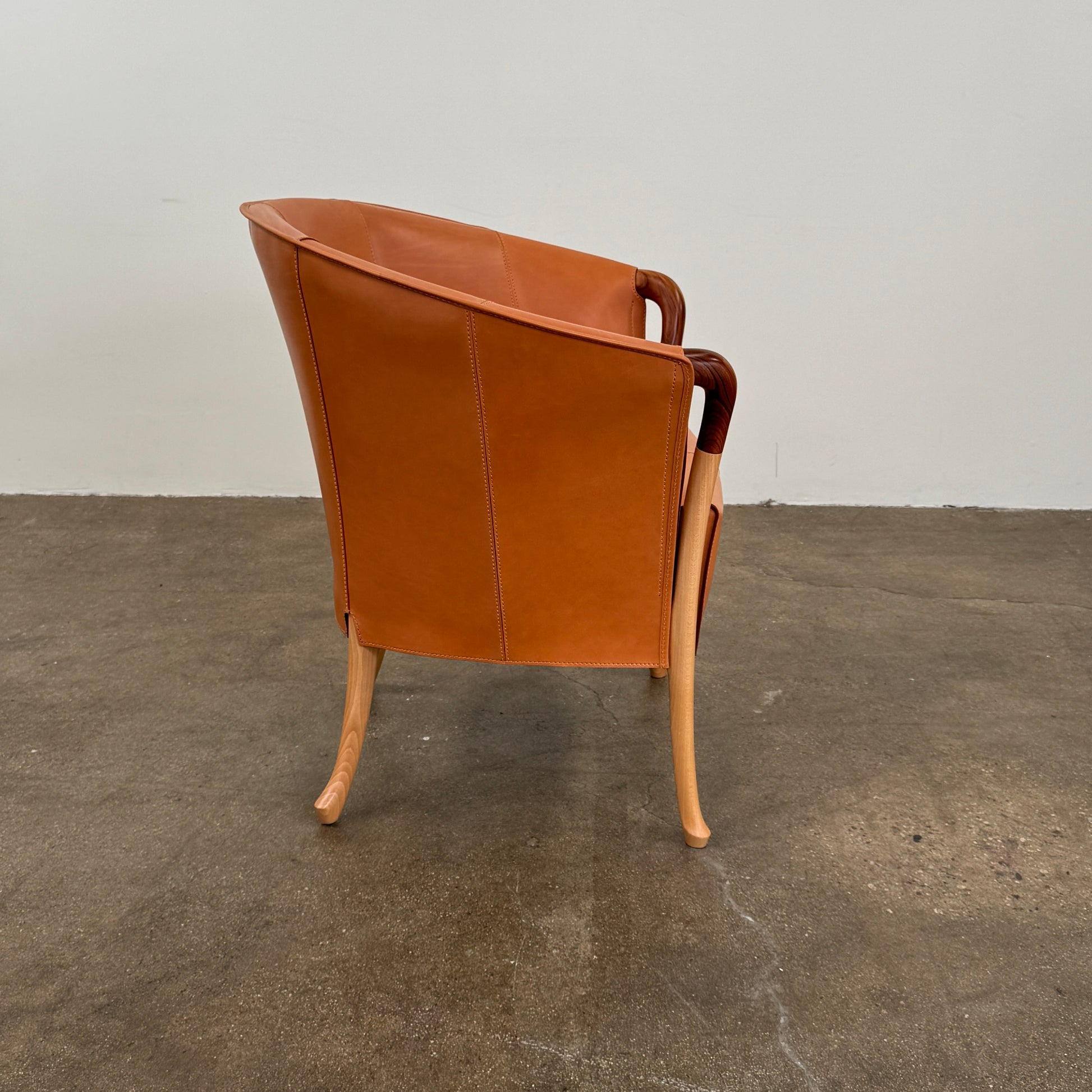 The Giorgetti “Progetti” Armchair by Giorgetti features a brown saddle leather seat, wooden legs, and Pau Ferro armrest accents, presented against a plain white background.