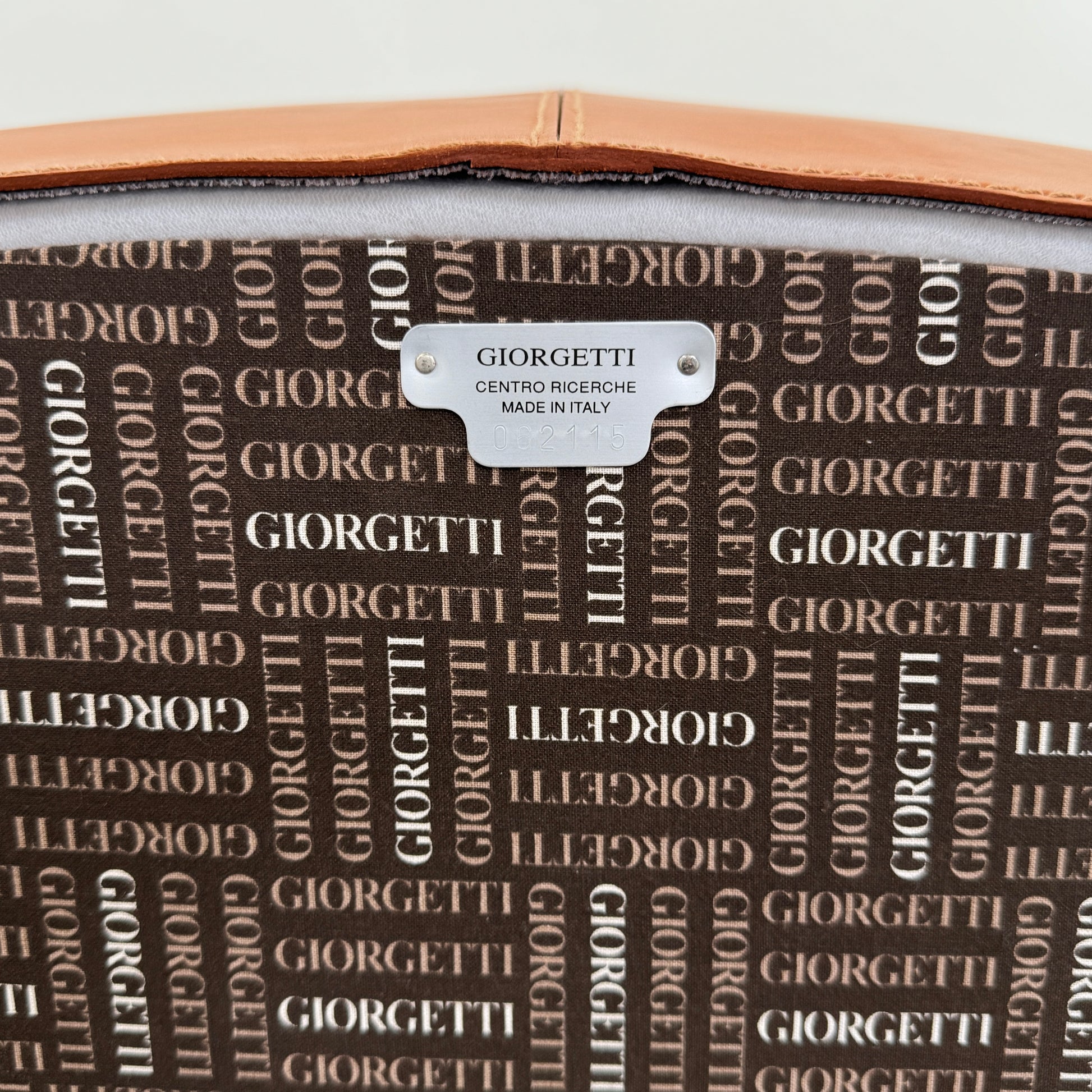 The Giorgetti “Progetti” Armchair by Giorgetti features a brown saddle leather seat, wooden legs, and Pau Ferro armrest accents, presented against a plain white background.