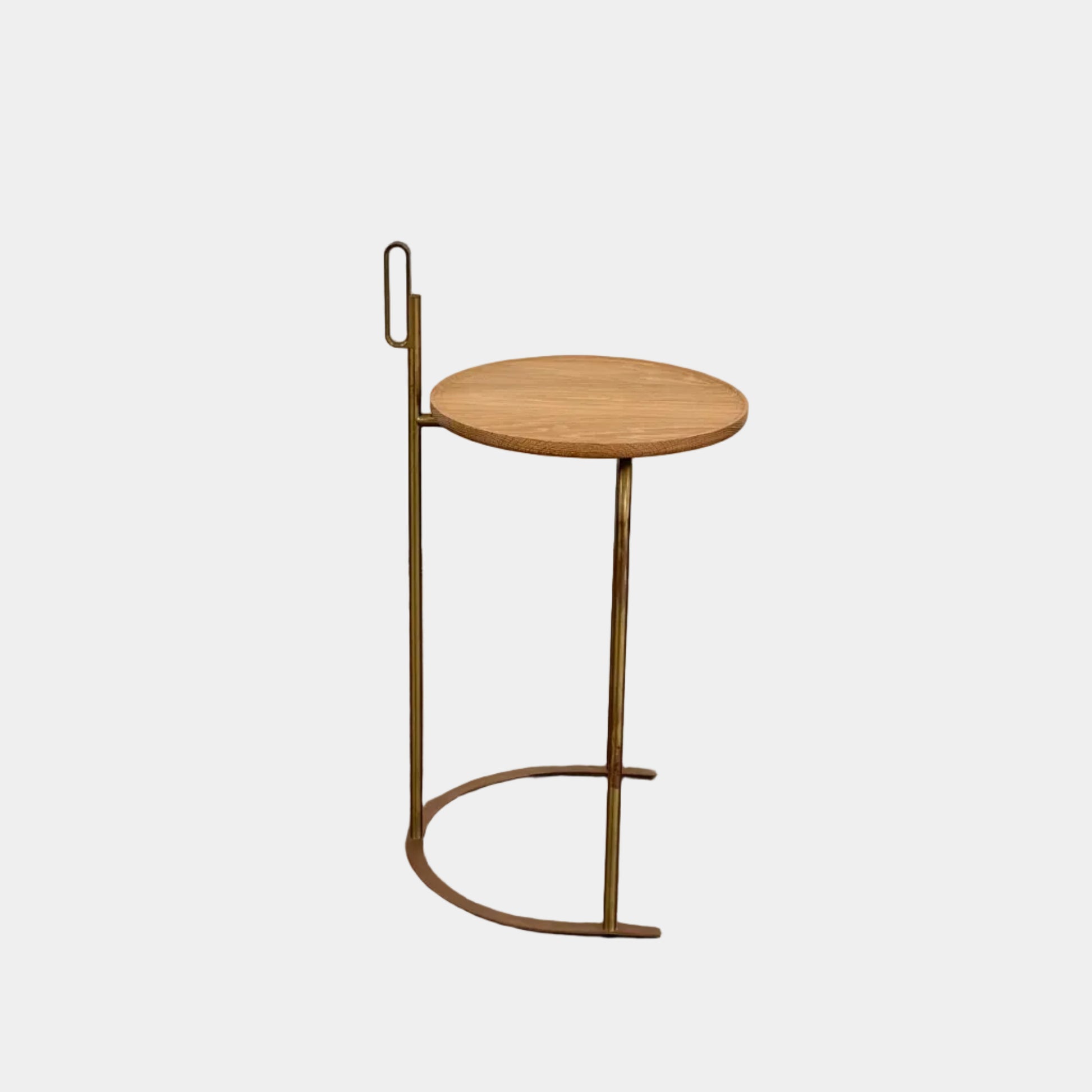 The De La Espada Handle Side Table by De La Espada features a small, round oiled oak top and a minimalist brass frame with a distinctive upright handle-like detail on one side.