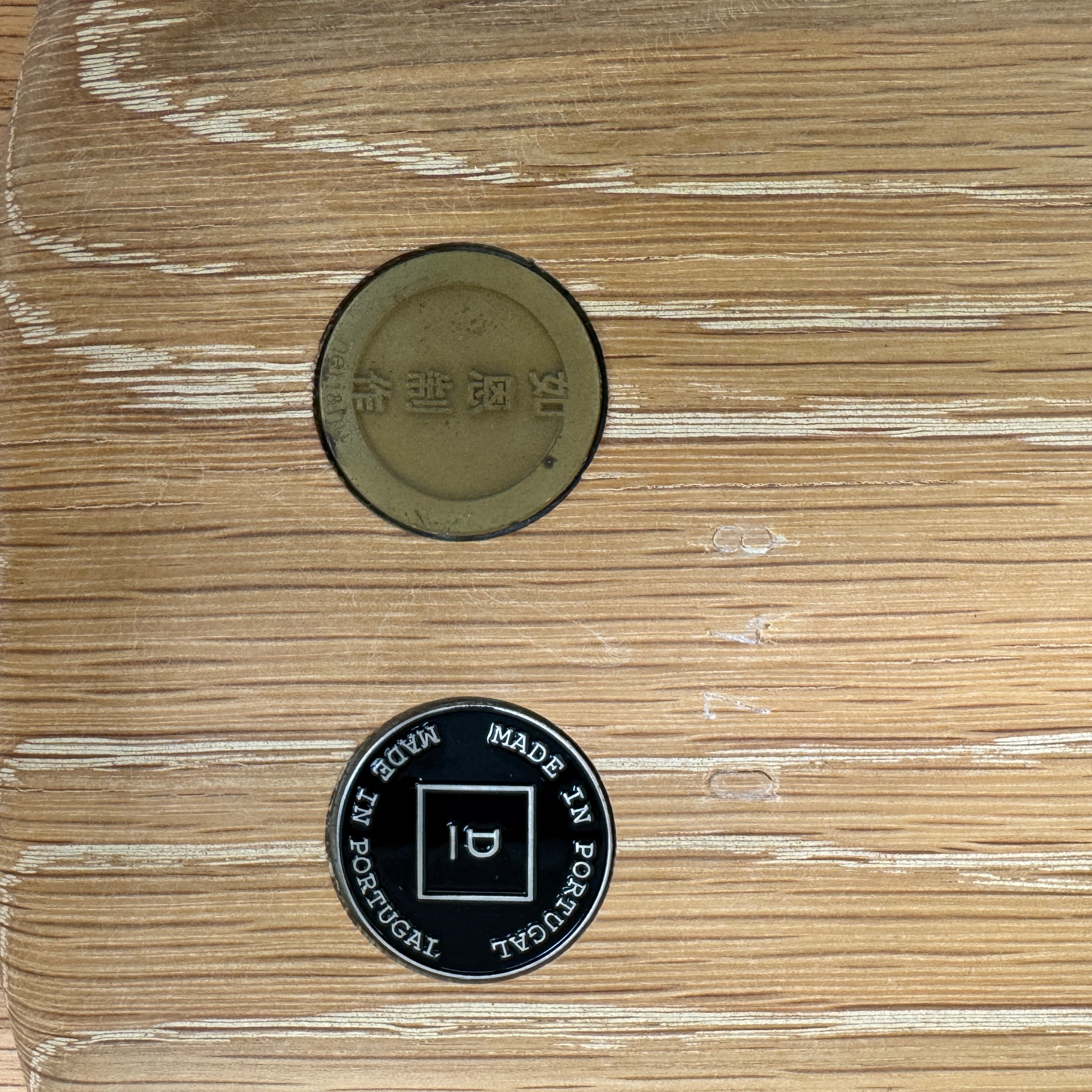 The De La Espada Handle Side Table by De La Espada features a small, round oiled oak top and a minimalist brass frame with a distinctive upright handle-like detail on one side.