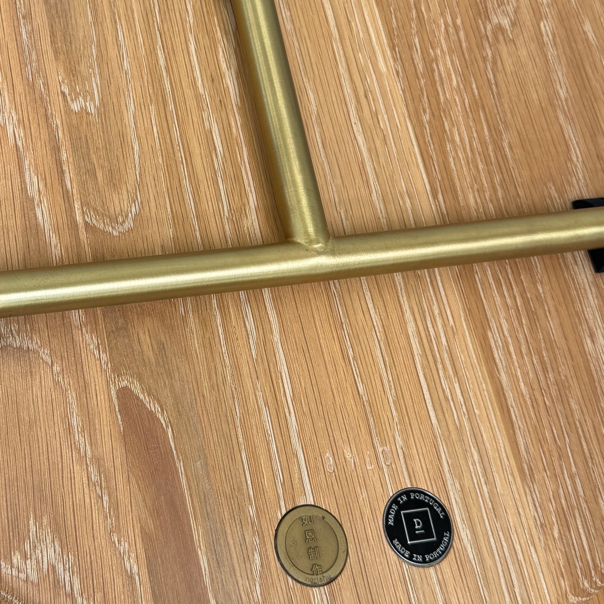 The De La Espada Handle Side Table by De La Espada features a small, round oiled oak top and a minimalist brass frame with a distinctive upright handle-like detail on one side.
