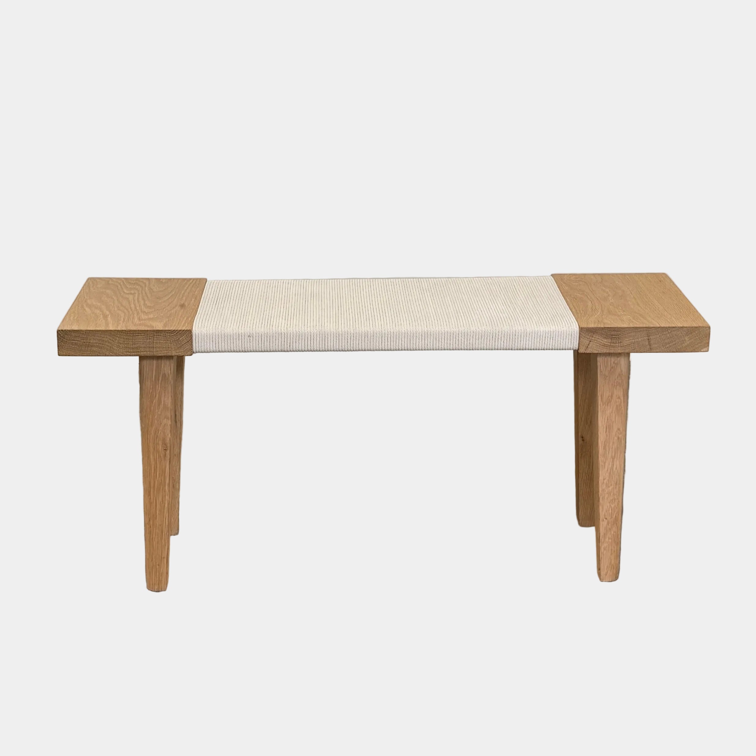 The Jenni Kayne Oak Day Bench by Jenni Kayne is a handcrafted White Oak piece with a minimalist design, featuring four legs and a light-colored woven seat, shown here on a polished concrete floor—an elegant addition to any Los Angeles furniture collection.