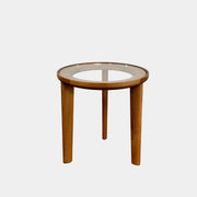 The DWR Port Side Table by DWR features a small, round design with three solid American oak legs and a clear glass top, shown against a plain white background.