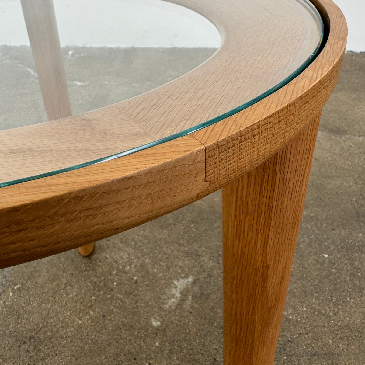 The DWR Port Side Table by DWR features a small, round design with three solid American oak legs and a clear glass top, shown against a plain white background.