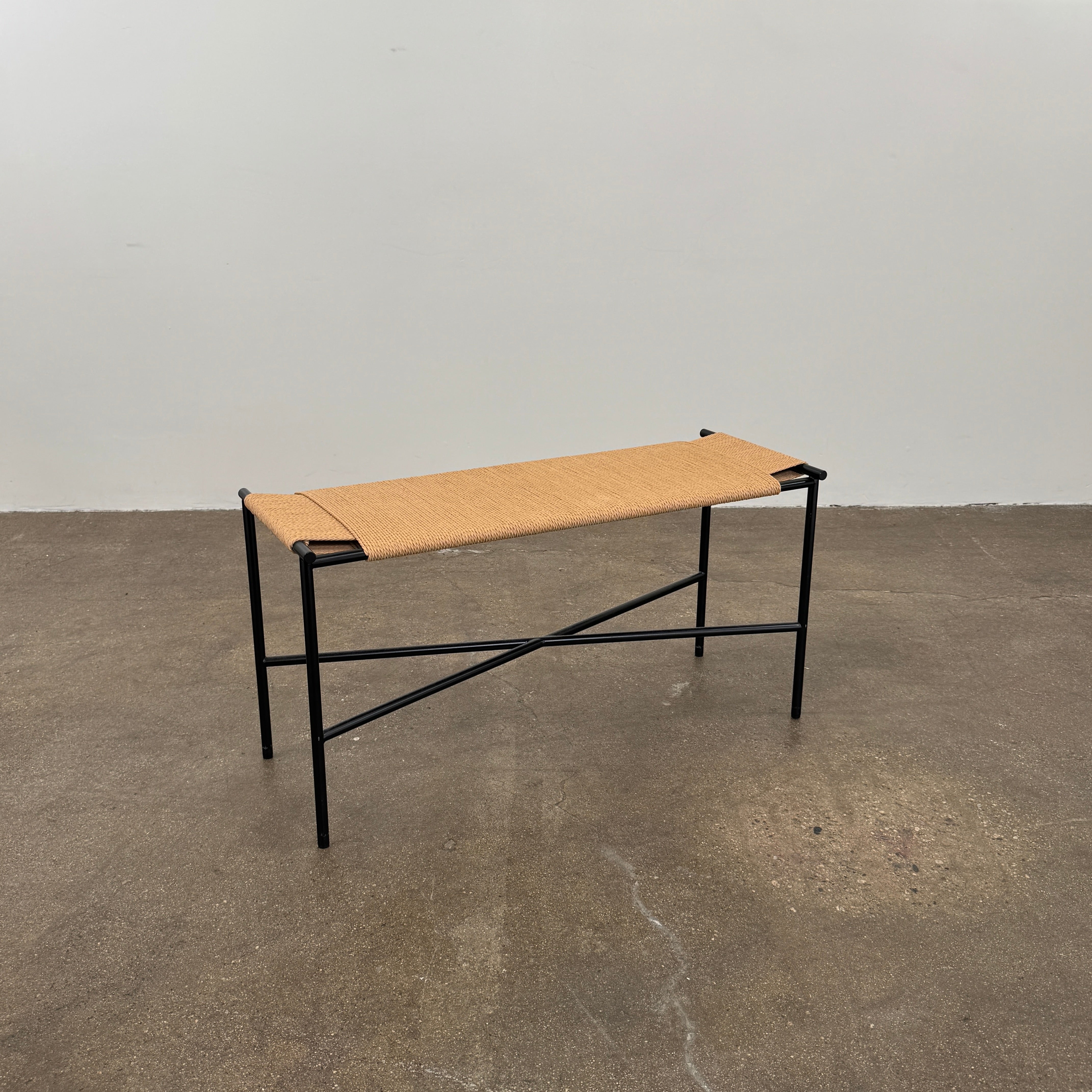 Fritz Hansen Skagerak VENT Bench by Fritz Hansen, featuring a rectangular black metal frame with minimalist crossed supports underneath and a woven tan paper cord seat, shown on a plain white background.