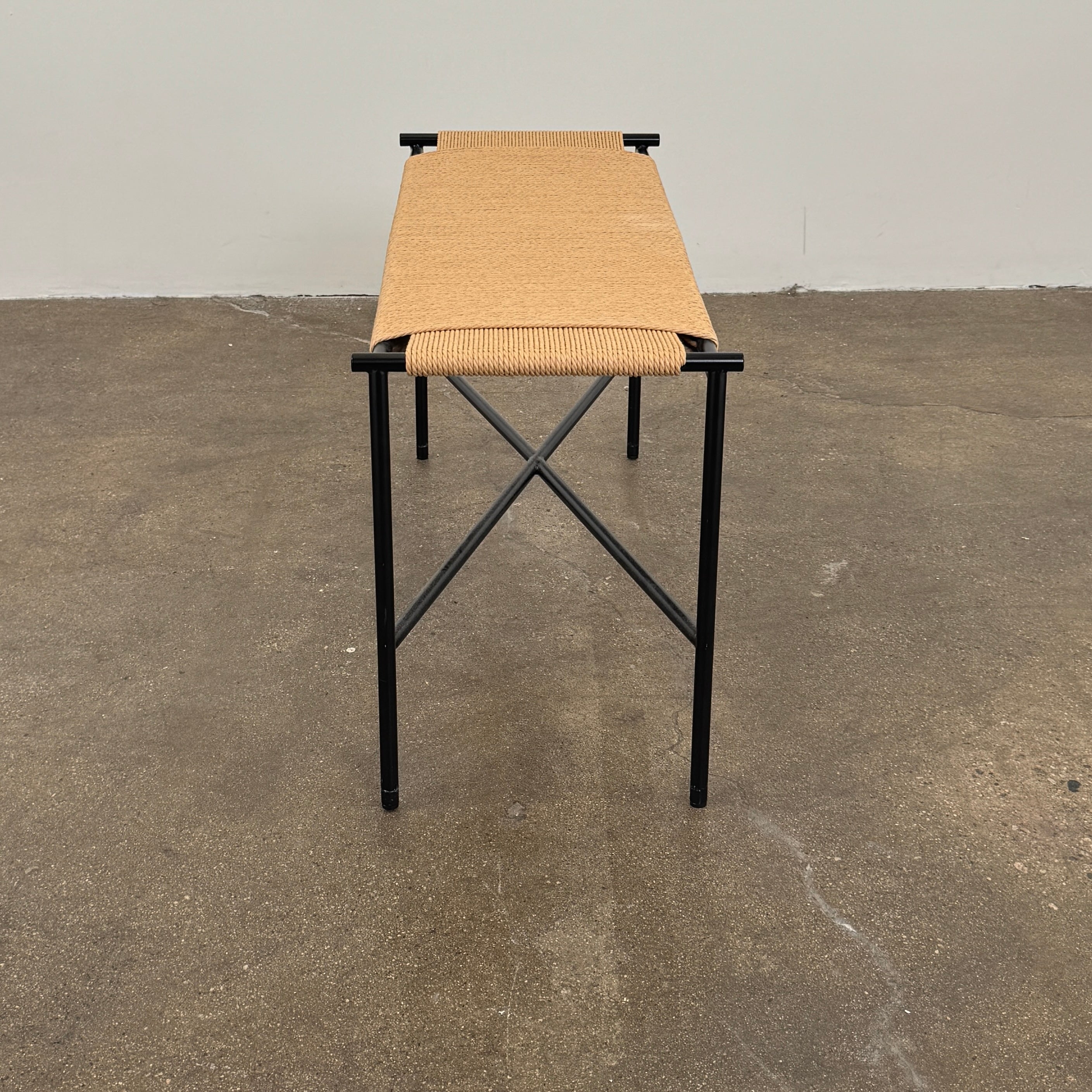 Fritz Hansen Skagerak VENT Bench by Fritz Hansen, featuring a rectangular black metal frame with minimalist crossed supports underneath and a woven tan paper cord seat, shown on a plain white background.