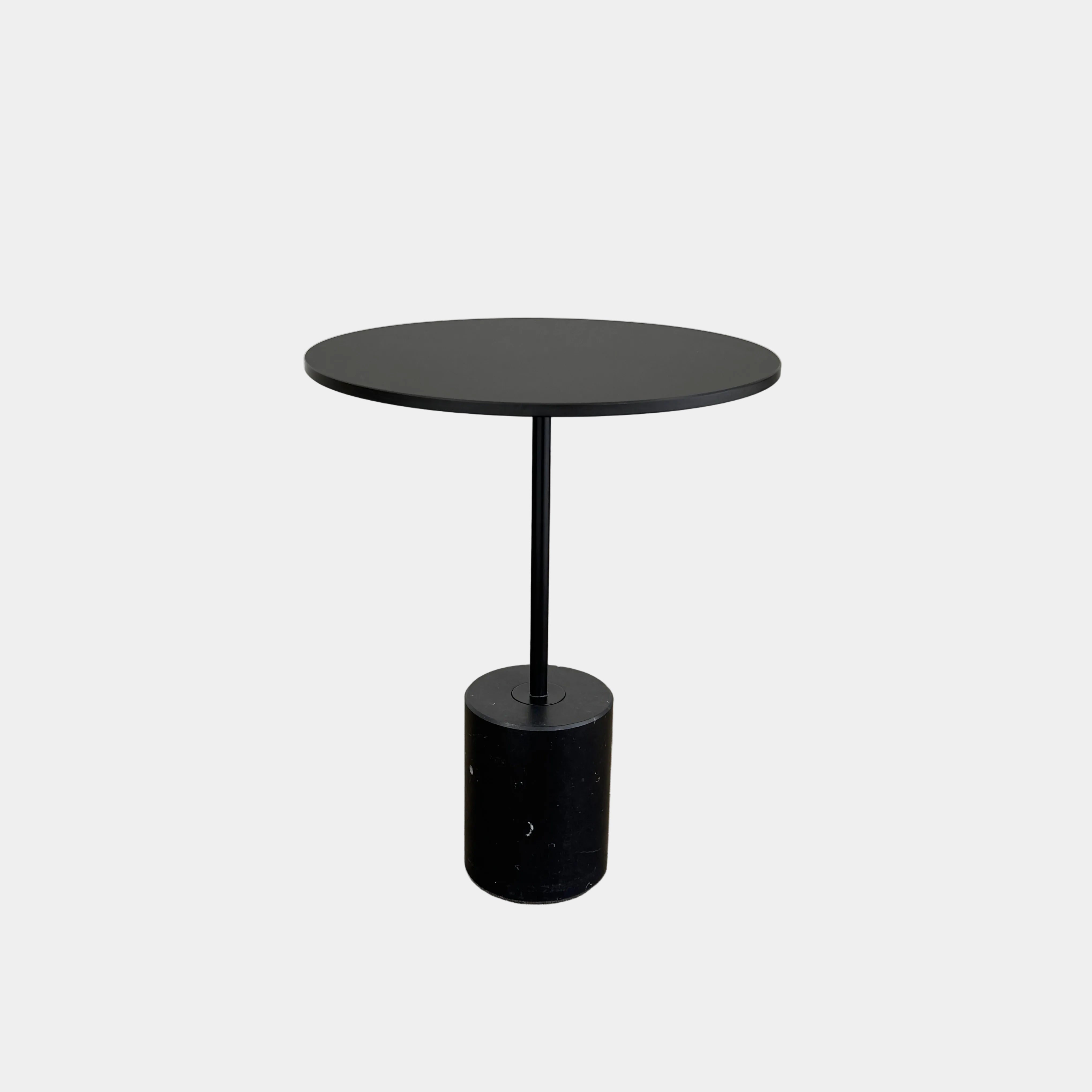 La Palma’s Jey Side Table features a minimalist black round top supported by a slim central column and anchored with a solid marble cylinder base, all showcased against a plain light background.