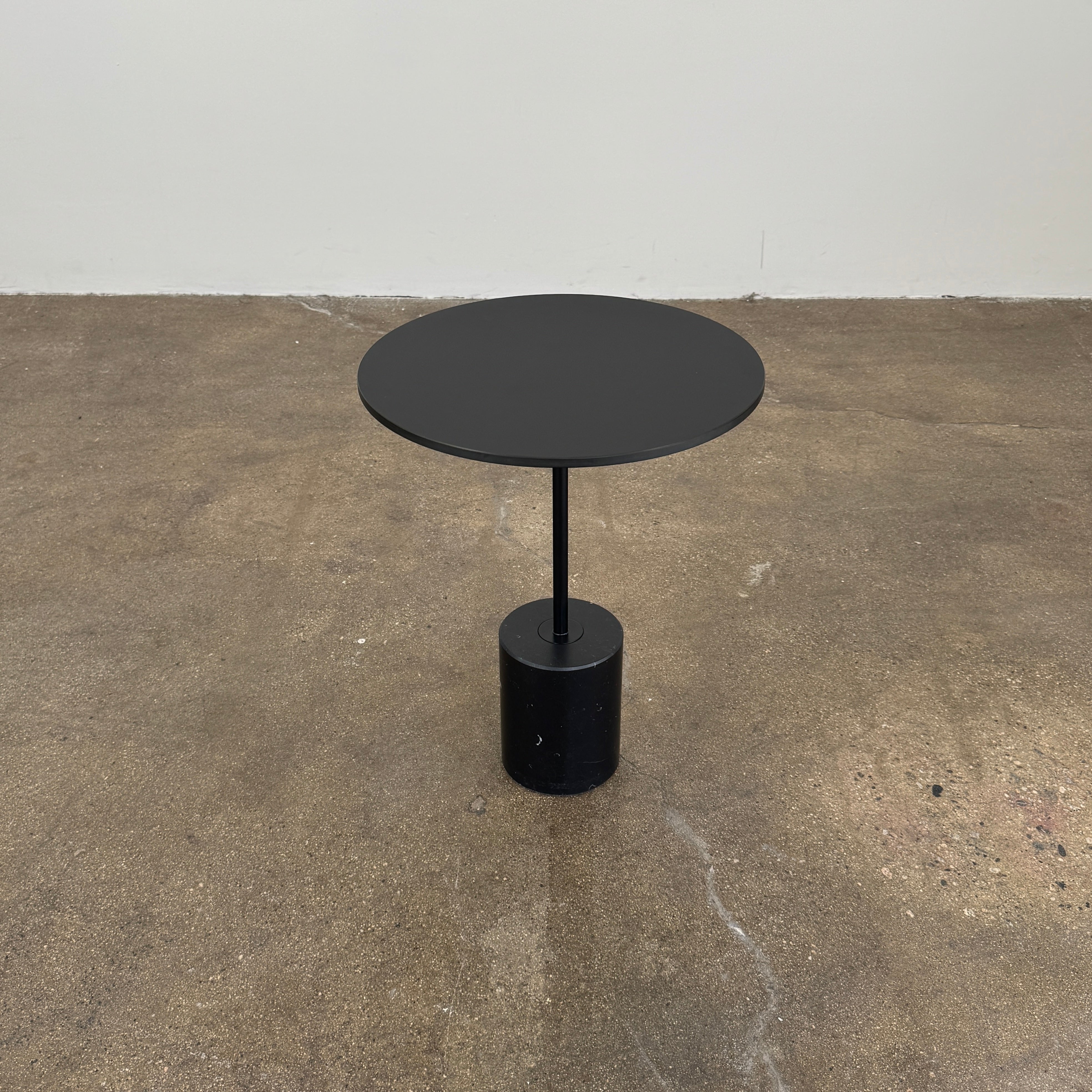 La Palma’s Jey Side Table features a minimalist black round top supported by a slim central column and anchored with a solid marble cylinder base, all showcased against a plain light background.