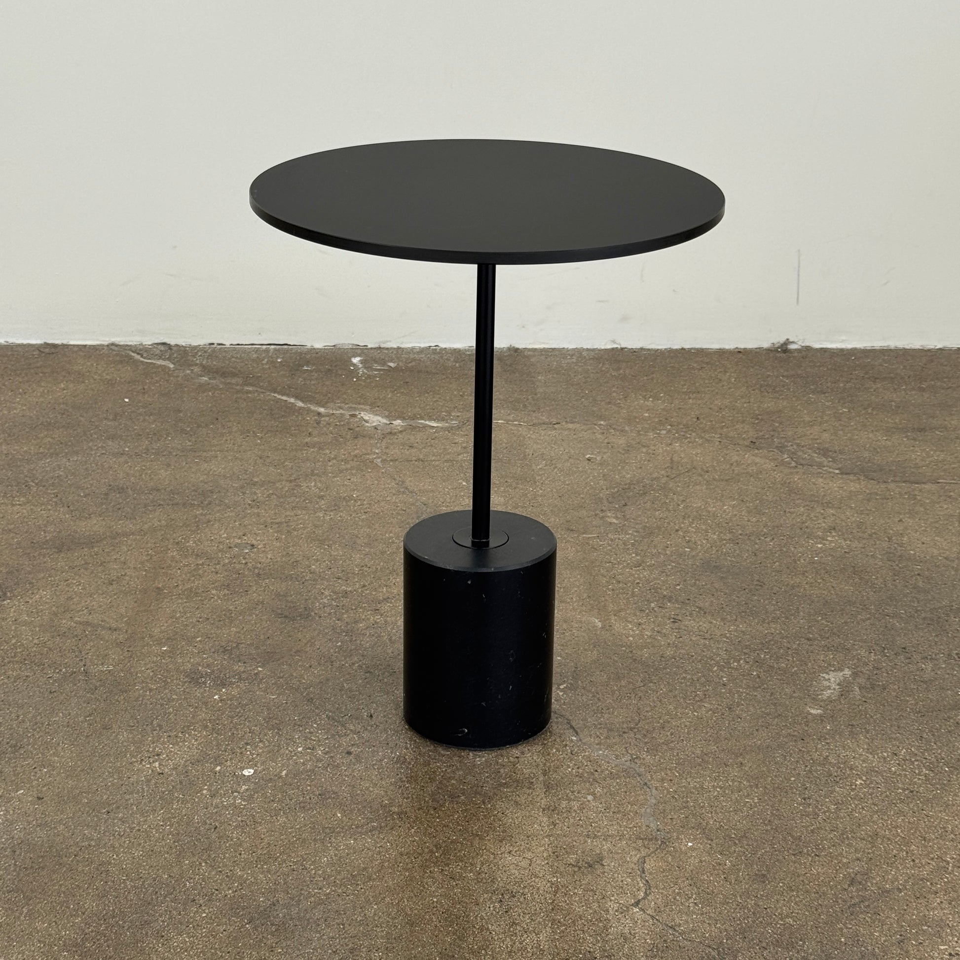 La Palma’s Jey Side Table features a minimalist black round top supported by a slim central column and anchored with a solid marble cylinder base, all showcased against a plain light background.