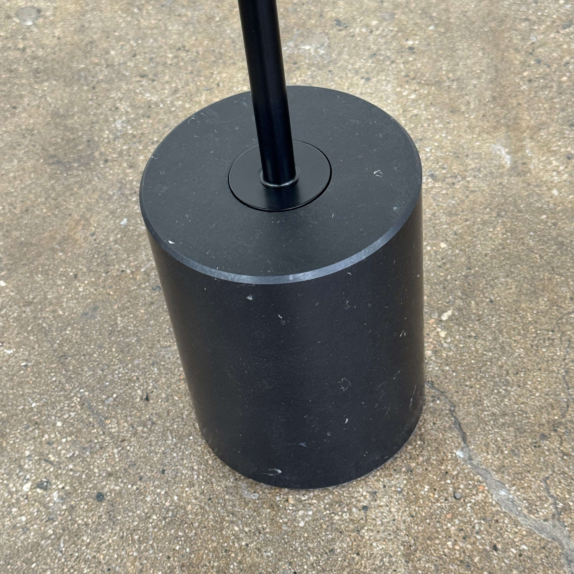 La Palma’s Jey Side Table features a minimalist black round top supported by a slim central column and anchored with a solid marble cylinder base, all showcased against a plain light background.