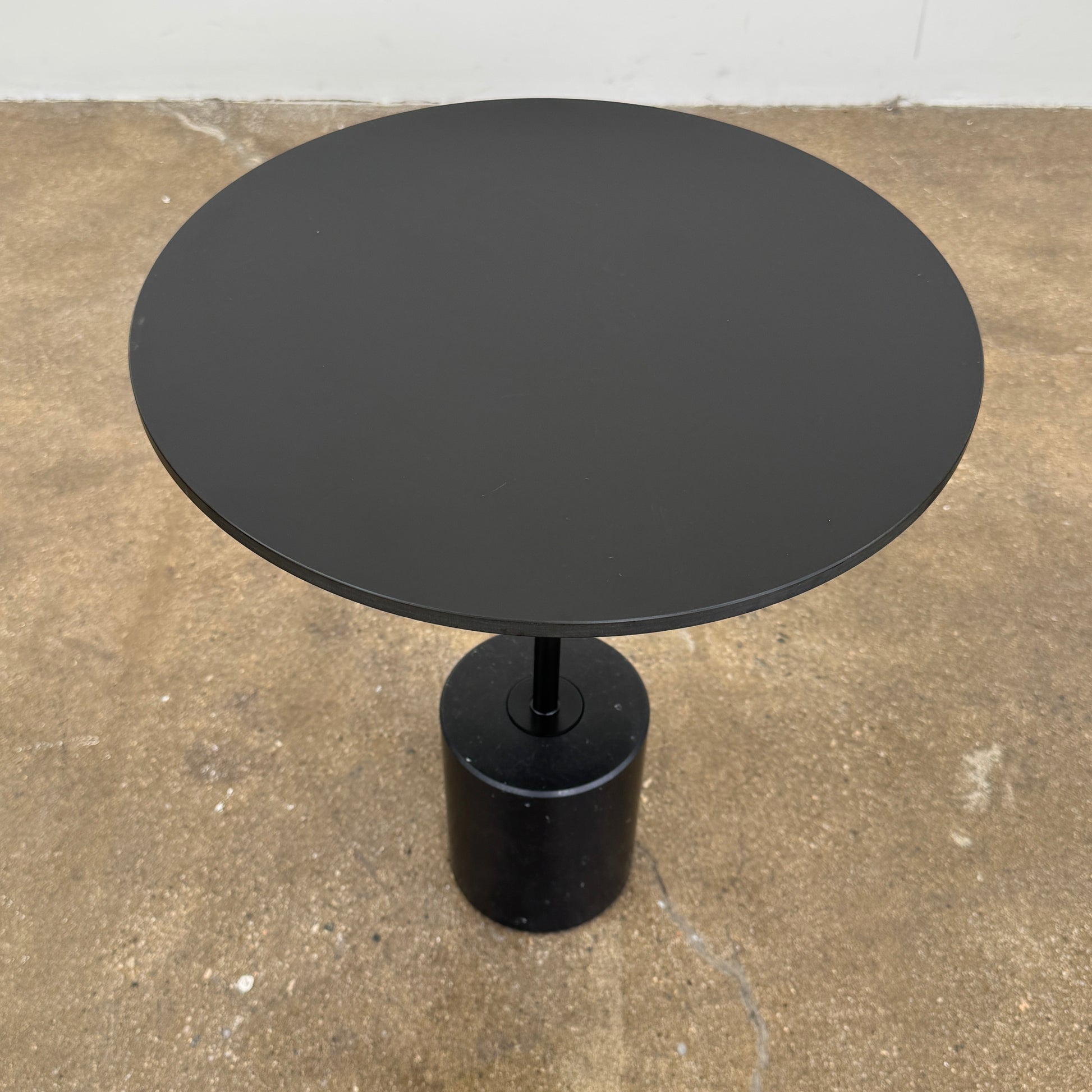 La Palma’s Jey Side Table features a minimalist black round top supported by a slim central column and anchored with a solid marble cylinder base, all showcased against a plain light background.