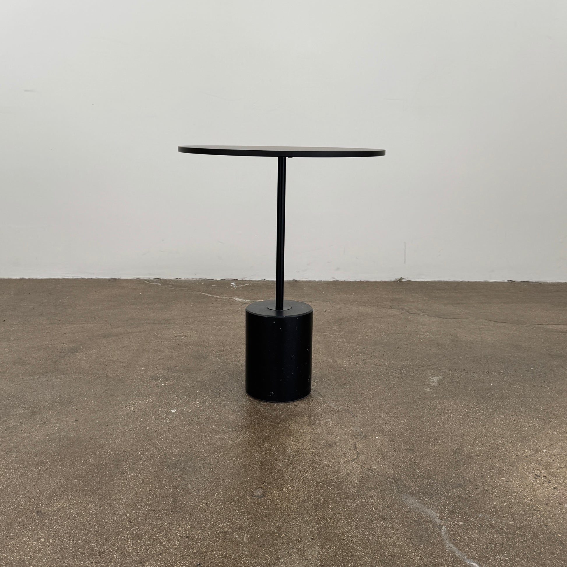 La Palma’s Jey Side Table features a minimalist black round top supported by a slim central column and anchored with a solid marble cylinder base, all showcased against a plain light background.