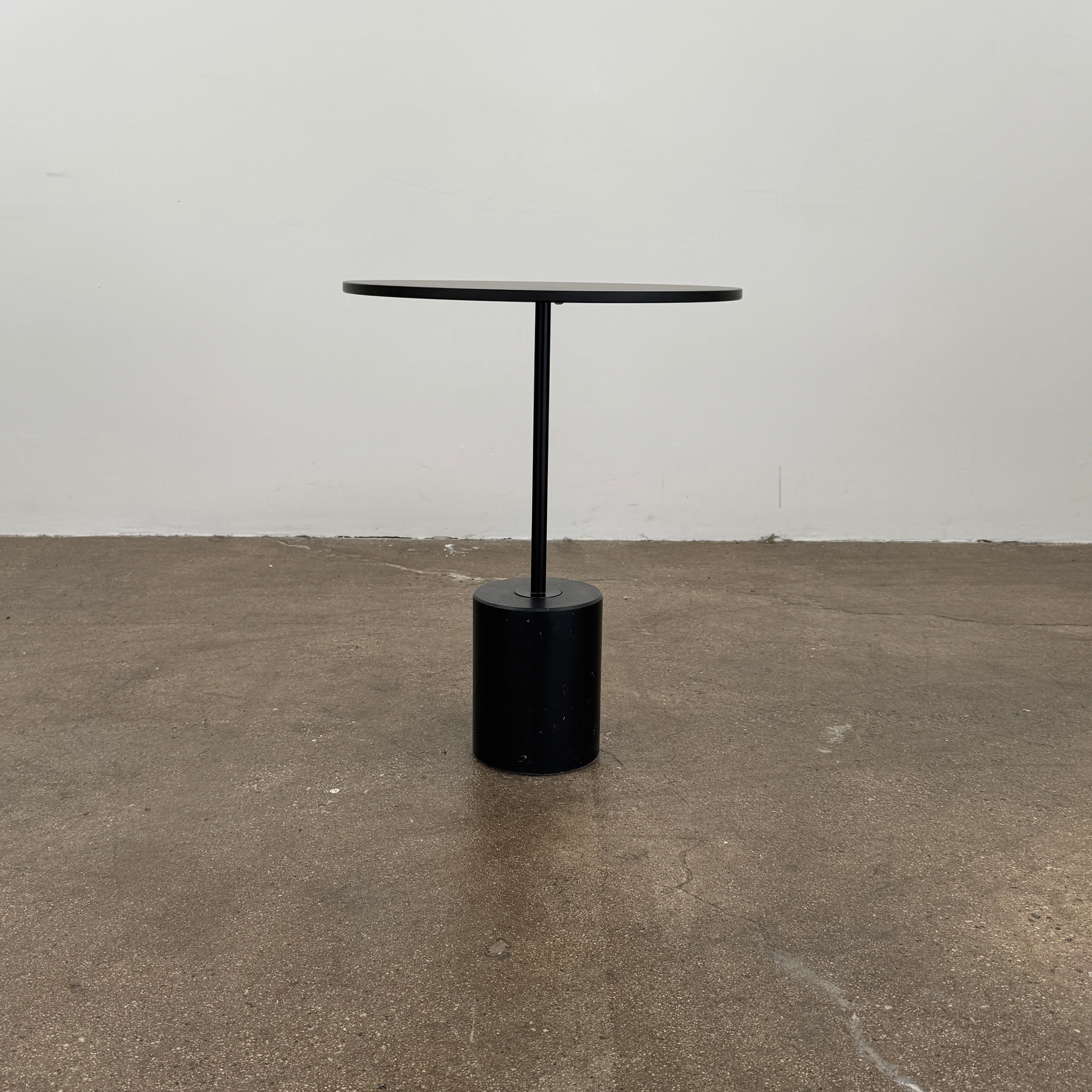 La Palma’s Jey Side Table features a minimalist black round top supported by a slim central column and anchored with a solid marble cylinder base, all showcased against a plain light background.