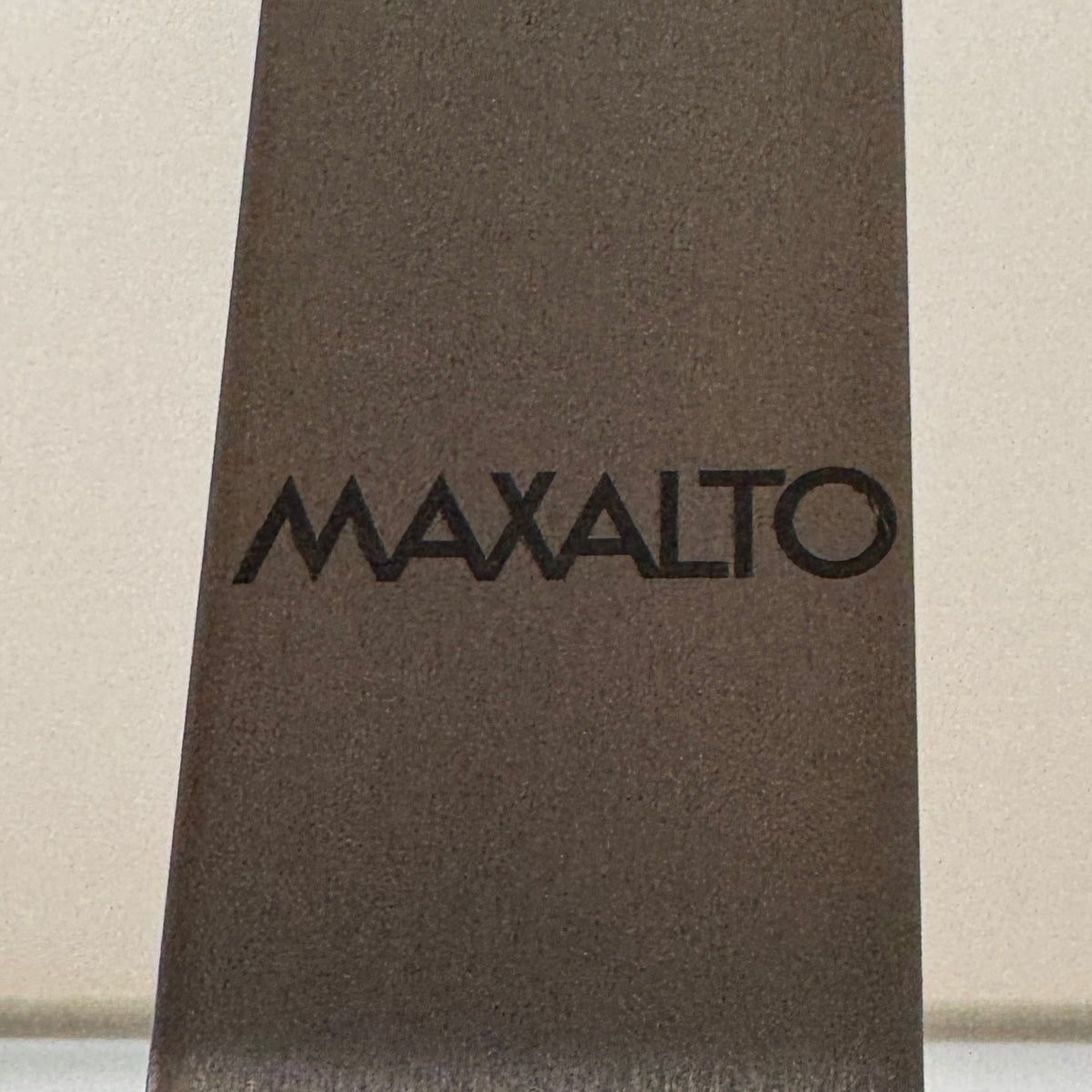 The Maxalto Leukon Tall Floor Lamp by Maxalto, featuring a minimalist design with a rectangular beige shade and a bronze nickel stand, stands on a bare concrete floor, plugged into an electrical outlet and casting ambient light throughout the space.