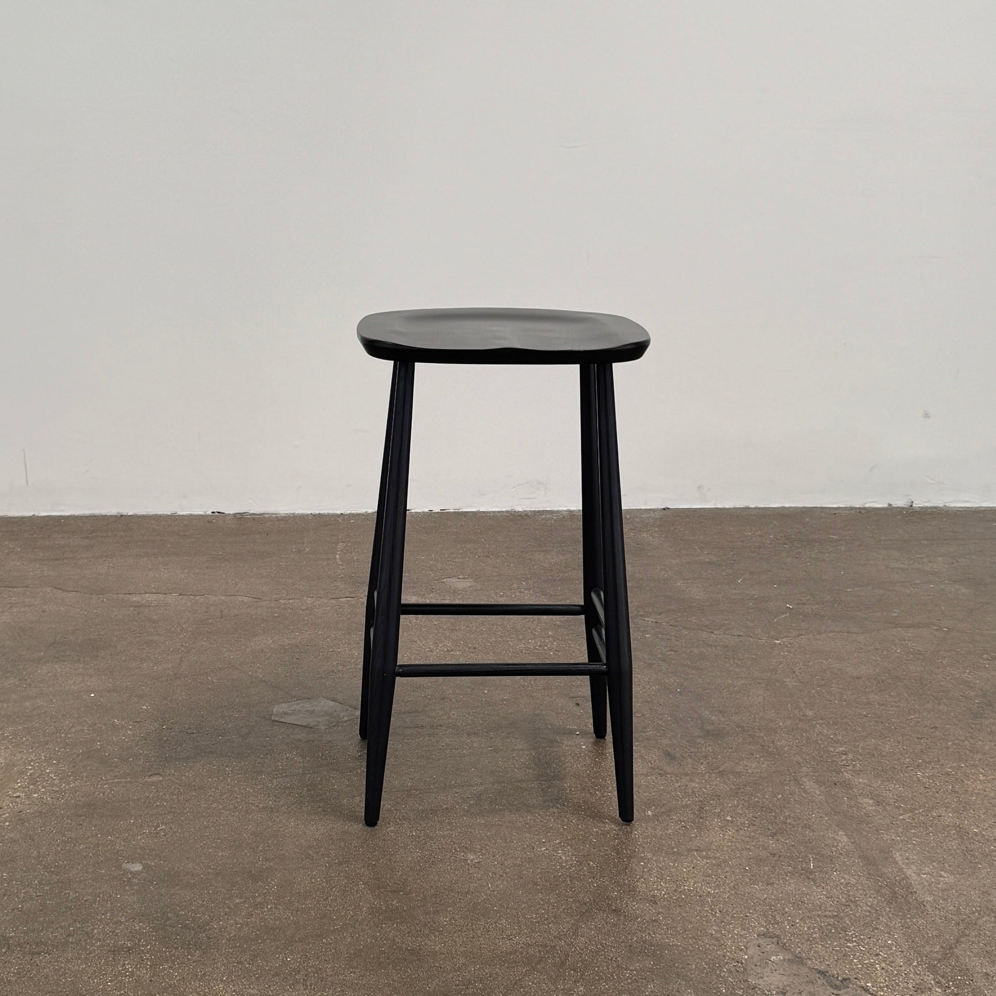 The Ercol Originals Counter Stool in Black Ash, crafted by Ercol, features four legs, a square contoured seat, and footrests on two sides. Set against a plain white background, this piece showcases the timeless craftsmanship of handmade British furniture.