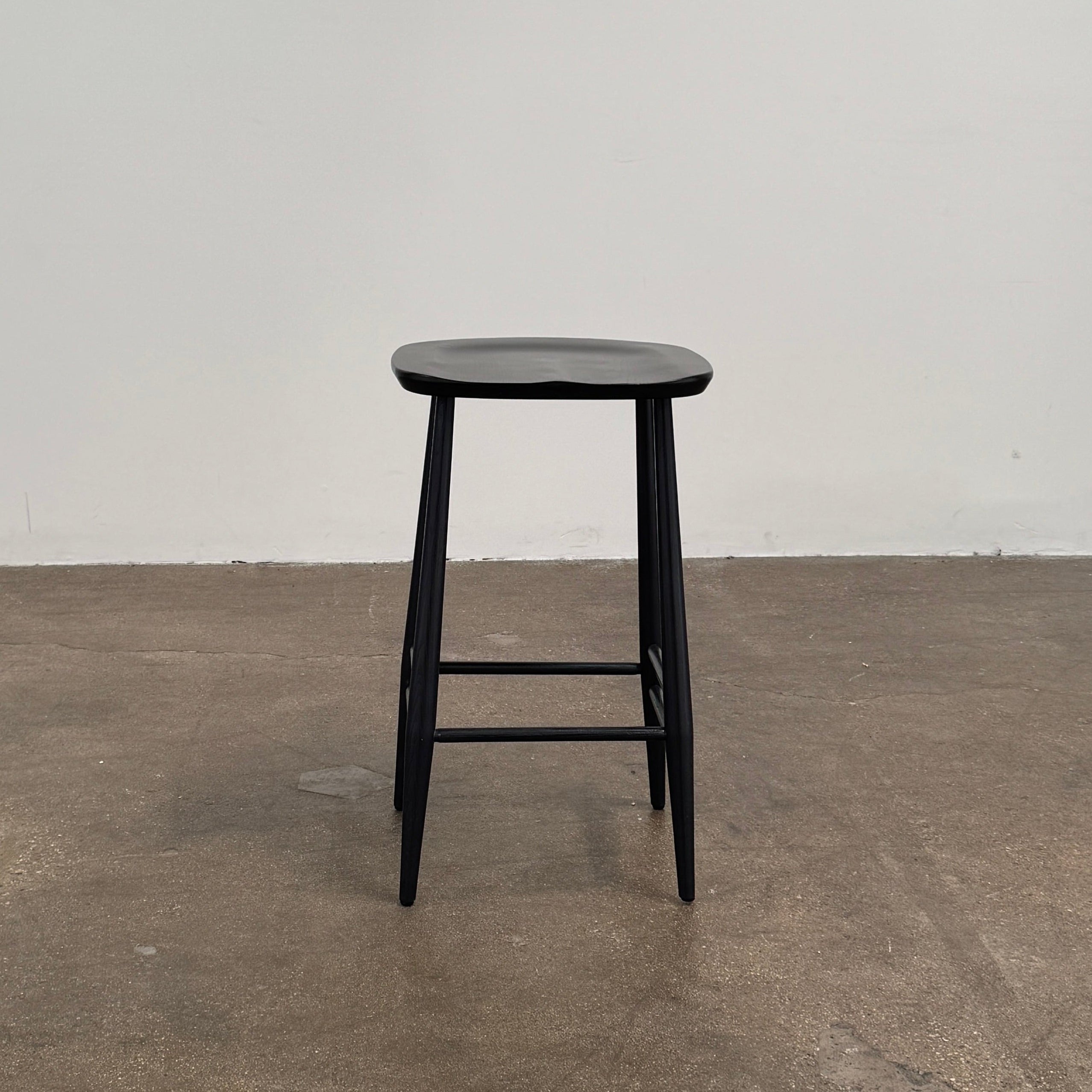 The Ercol Originals Counter Stool in Black Ash, crafted by Ercol, features four legs, a square contoured seat, and footrests on two sides. Set against a plain white background, this piece showcases the timeless craftsmanship of handmade British furniture.
