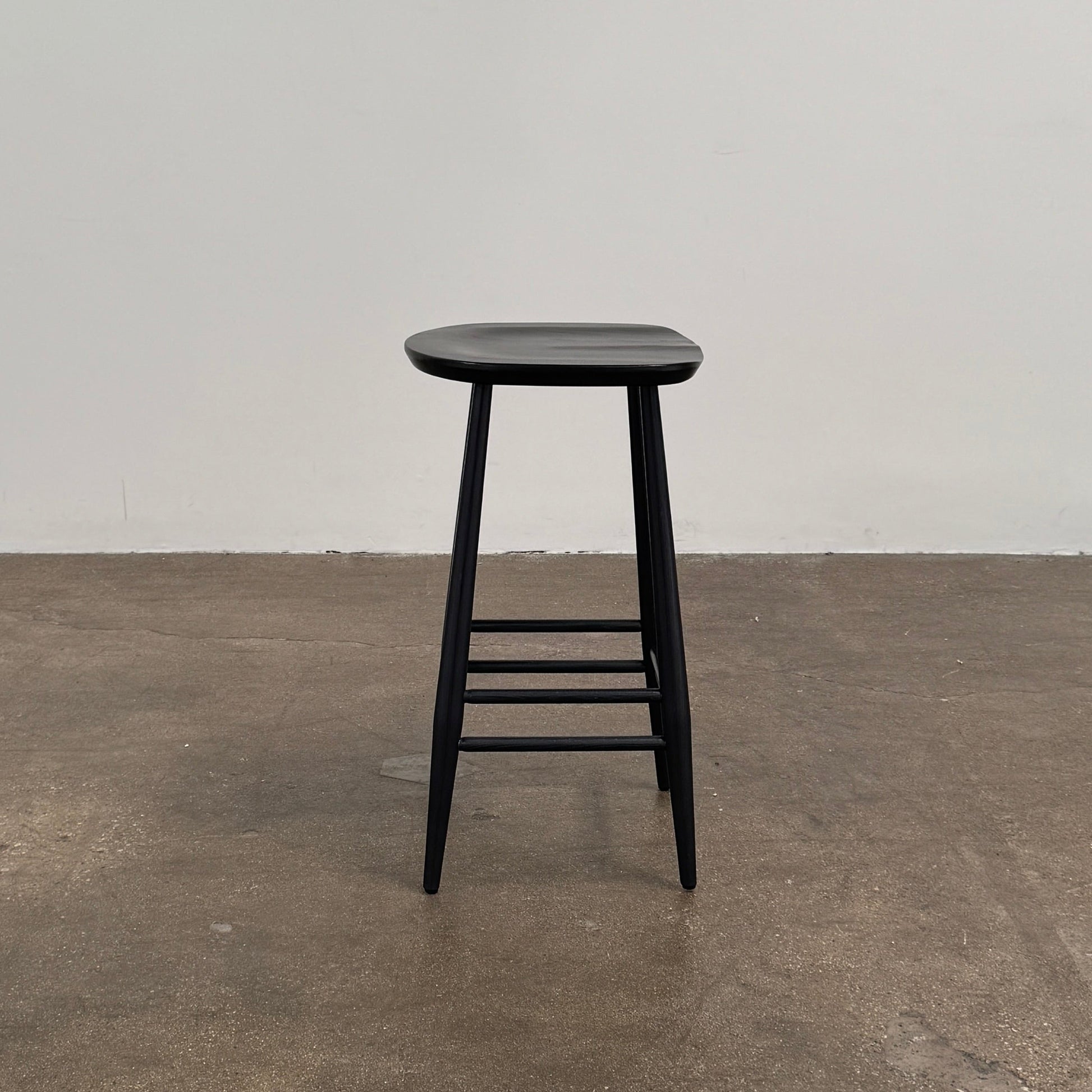 The Ercol Originals Counter Stool in Black Ash, crafted by Ercol, features four legs, a square contoured seat, and footrests on two sides. Set against a plain white background, this piece showcases the timeless craftsmanship of handmade British furniture.
