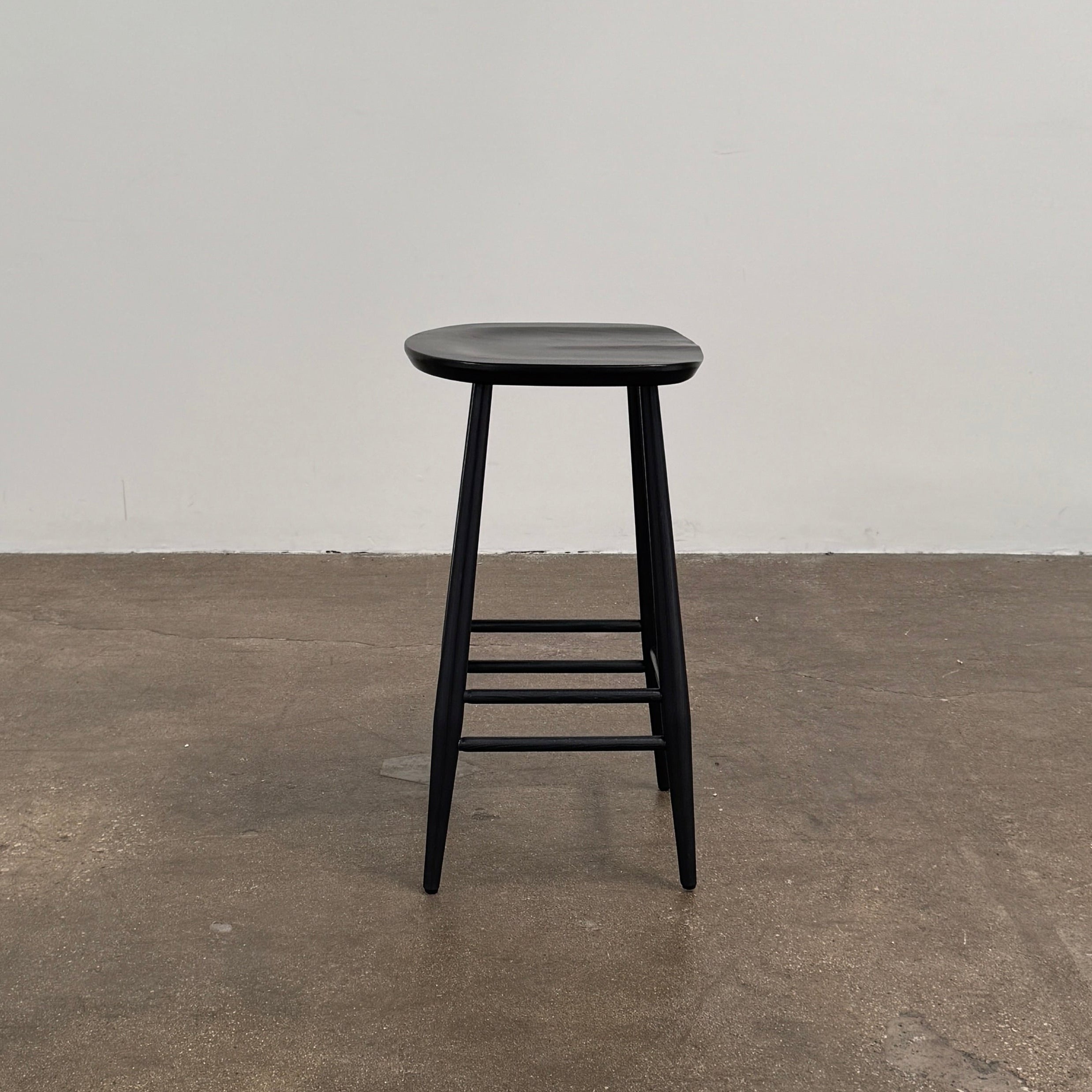 The Ercol Originals Counter Stool in Black Ash, crafted by Ercol, features four legs, a square contoured seat, and footrests on two sides. Set against a plain white background, this piece showcases the timeless craftsmanship of handmade British furniture.