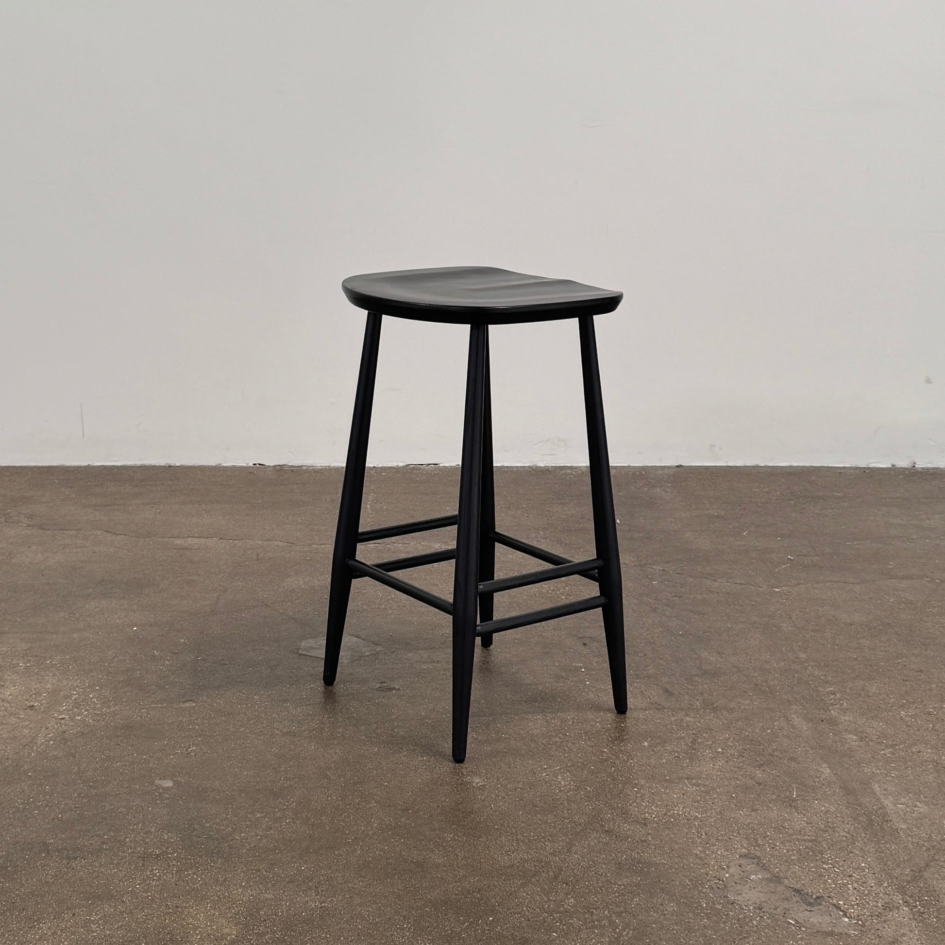 The Ercol Originals Counter Stool in Black Ash, crafted by Ercol, features four legs, a square contoured seat, and footrests on two sides. Set against a plain white background, this piece showcases the timeless craftsmanship of handmade British furniture.