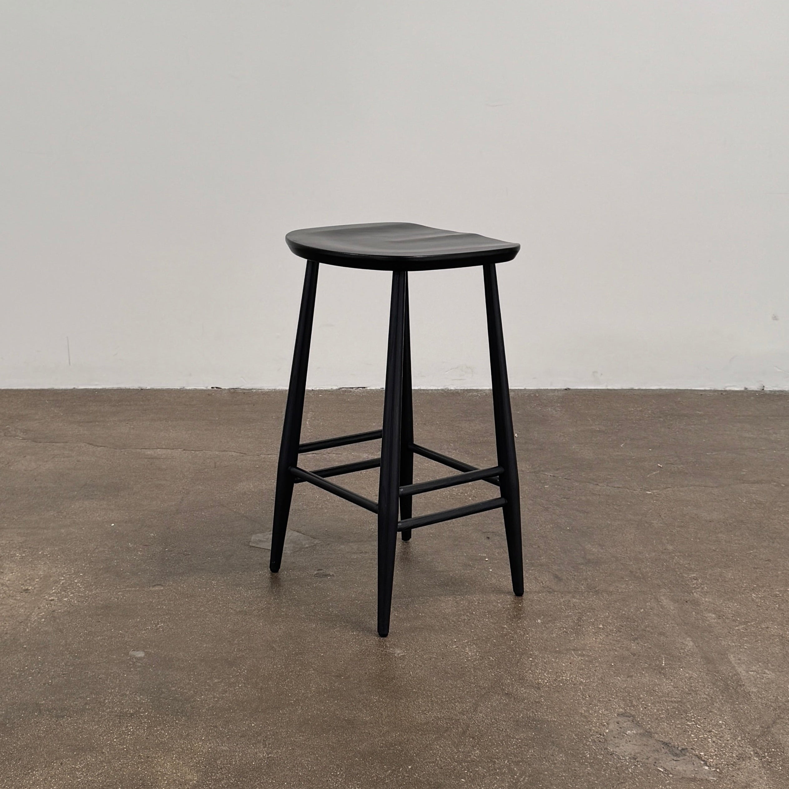 The Ercol Originals Counter Stool in Black Ash, crafted by Ercol, features four legs, a square contoured seat, and footrests on two sides. Set against a plain white background, this piece showcases the timeless craftsmanship of handmade British furniture.