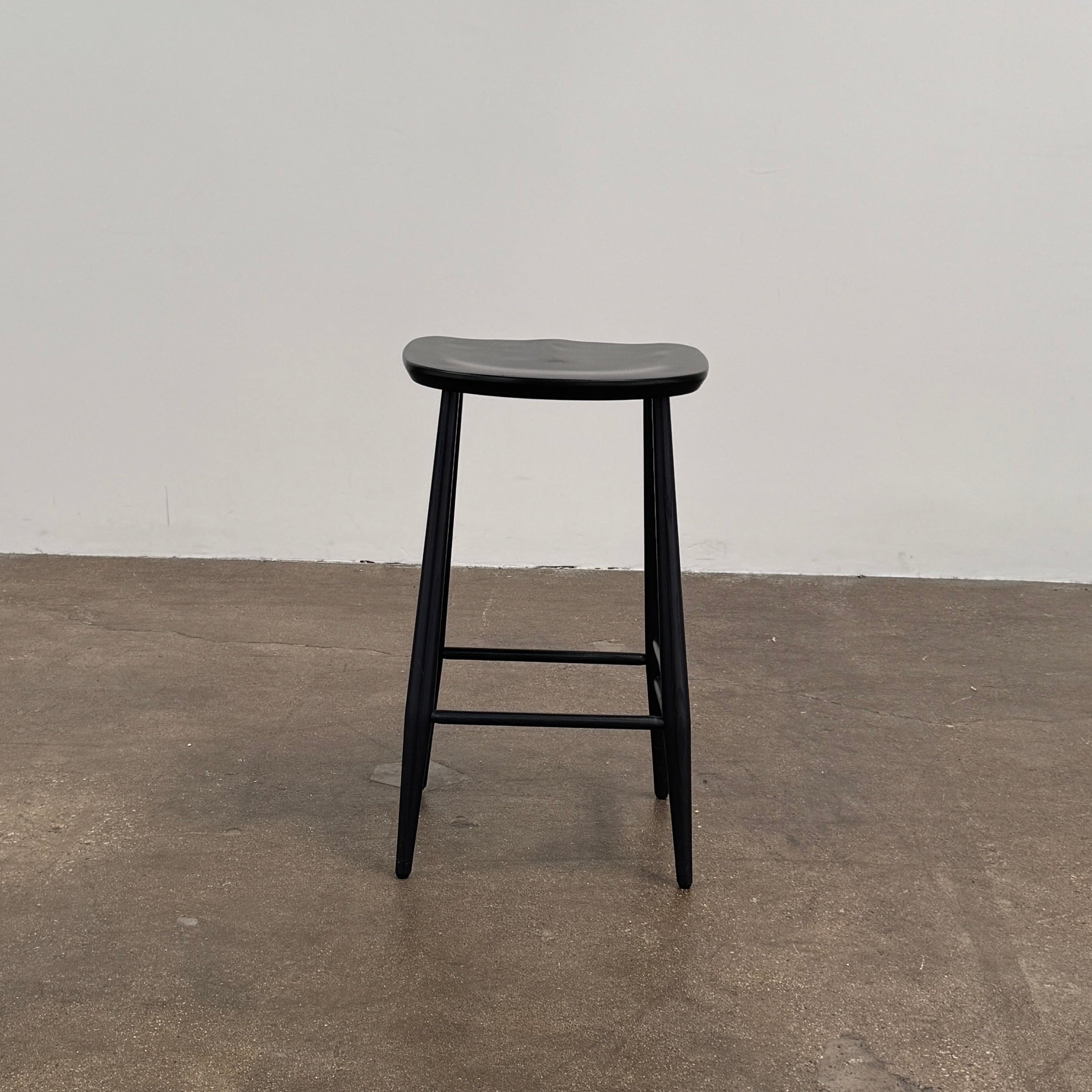 The Ercol Originals Counter Stool in Black Ash, crafted by Ercol, features four legs, a square contoured seat, and footrests on two sides. Set against a plain white background, this piece showcases the timeless craftsmanship of handmade British furniture.