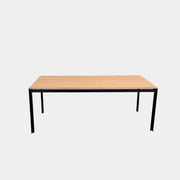 A PK52 Professor Desk by Poul Kjaerholm for Carl Hansen & Son, featuring a rectangular wooden top and black metal legs, stands on a brown concrete floor against a plain white wall.