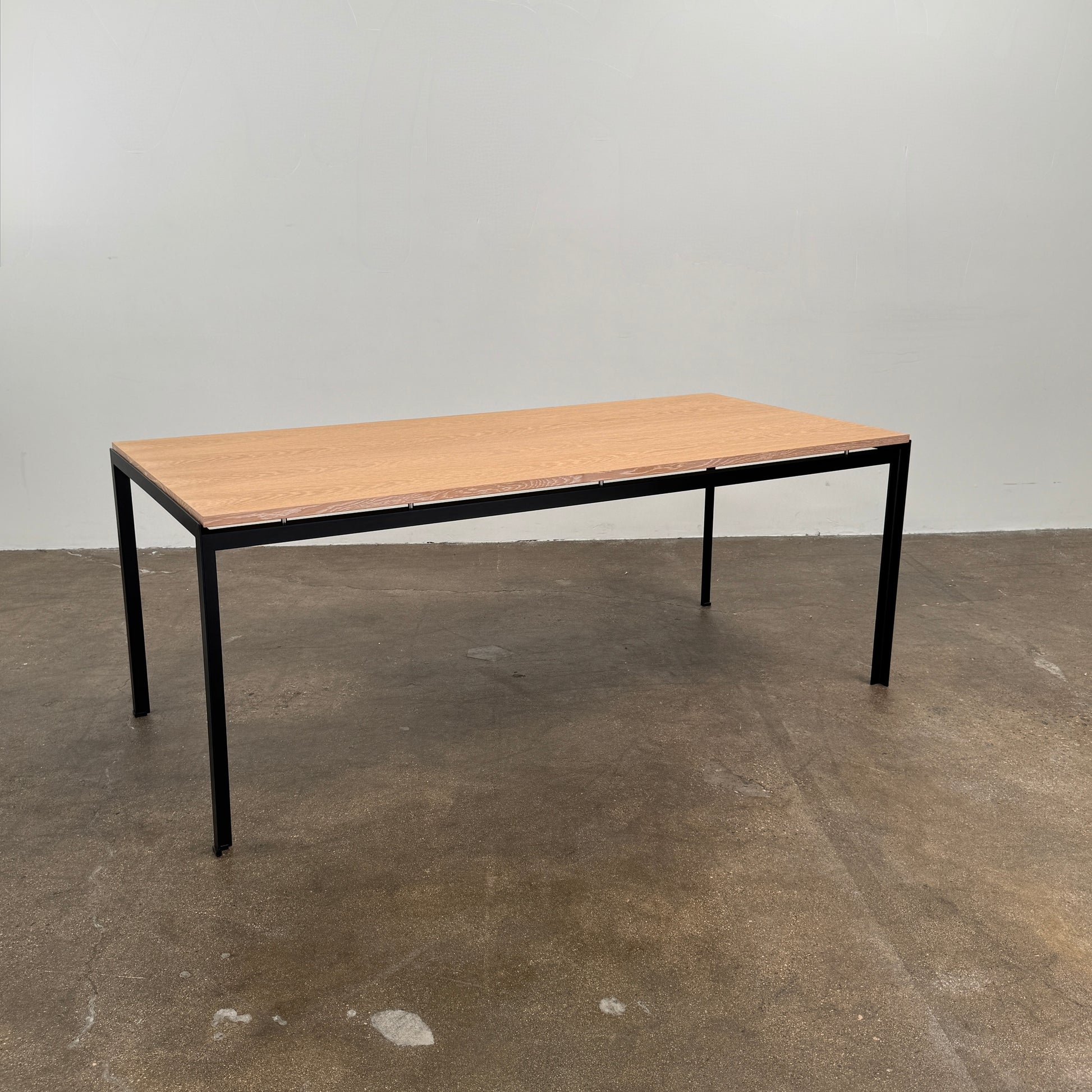 A PK52 Professor Desk by Poul Kjaerholm for Carl Hansen & Son, featuring a rectangular wooden top and black metal legs, stands on a brown concrete floor against a plain white wall.
