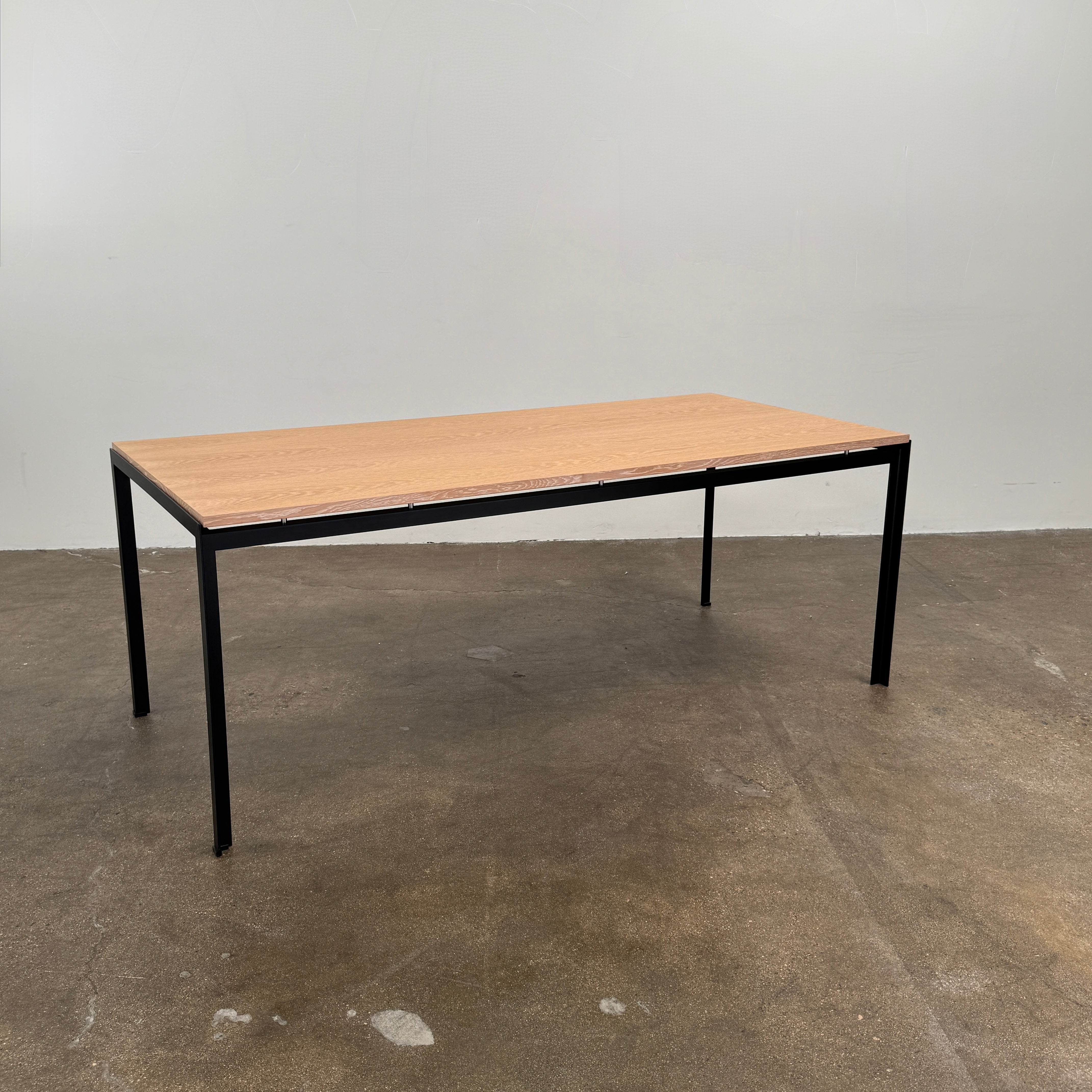 A PK52 Professor Desk by Poul Kjaerholm for Carl Hansen & Son, featuring a rectangular wooden top and black metal legs, stands on a brown concrete floor against a plain white wall.