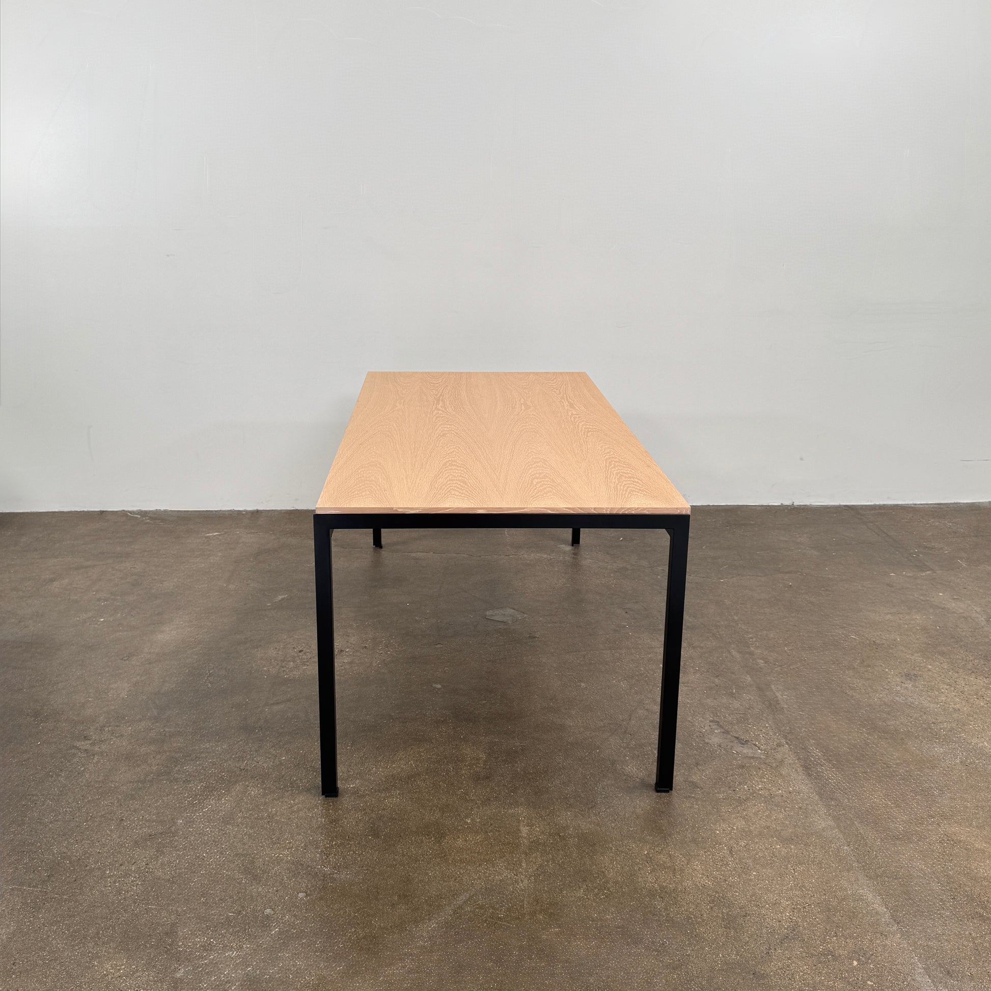 A PK52 Professor Desk by Poul Kjaerholm for Carl Hansen & Son, featuring a rectangular wooden top and black metal legs, stands on a brown concrete floor against a plain white wall.