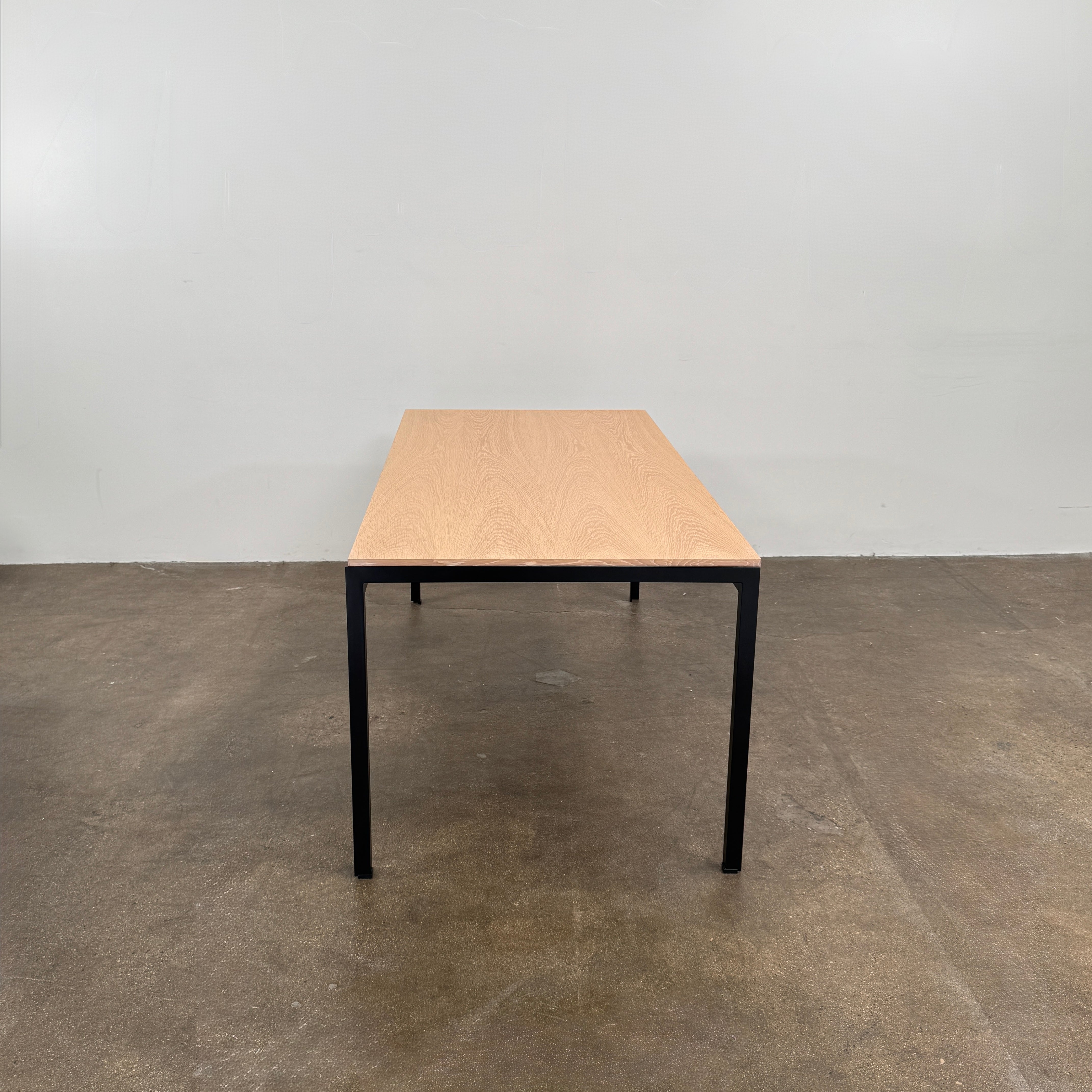 A PK52 Professor Desk by Poul Kjaerholm for Carl Hansen & Son, featuring a rectangular wooden top and black metal legs, stands on a brown concrete floor against a plain white wall.