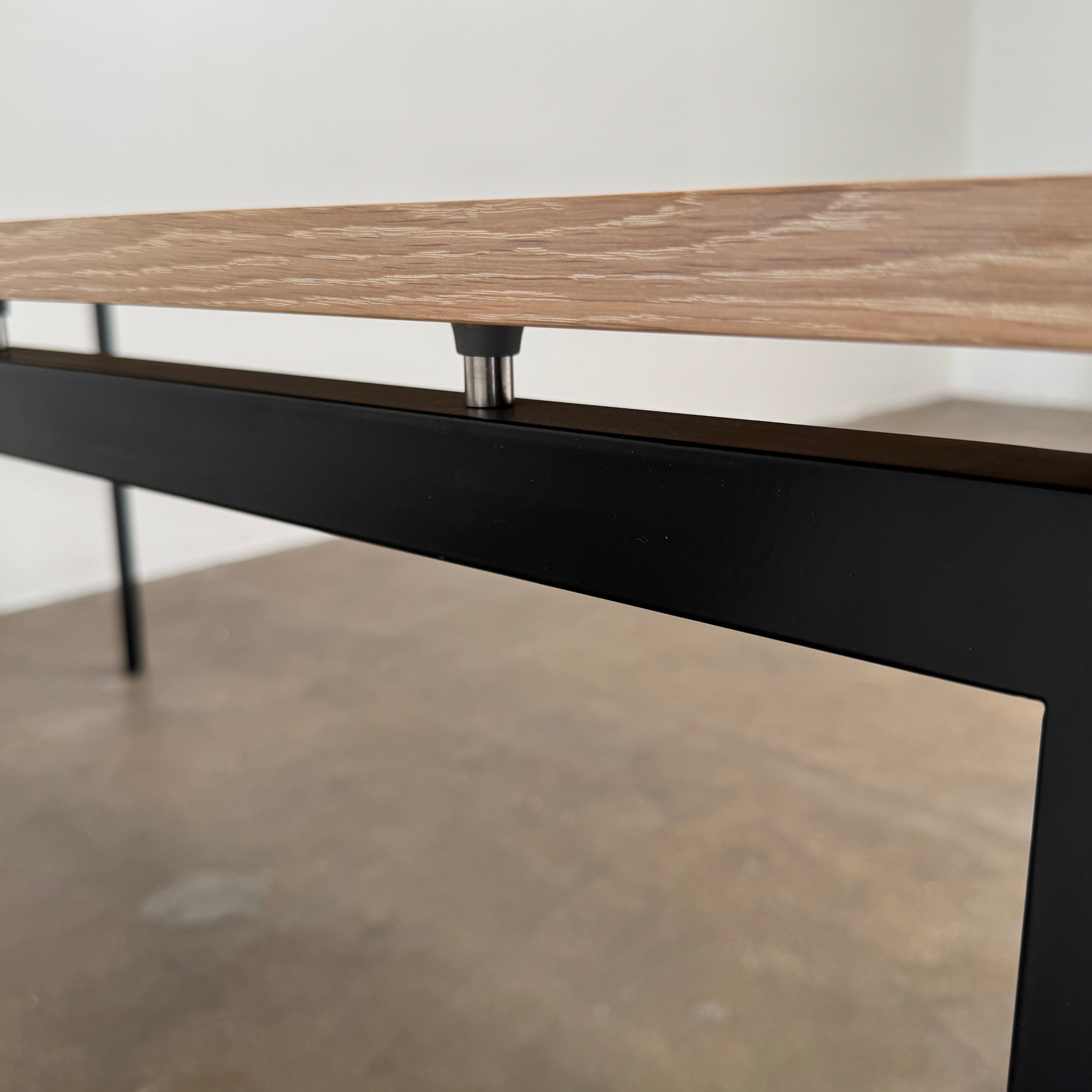 A PK52 Professor Desk by Poul Kjaerholm for Carl Hansen & Son, featuring a rectangular wooden top and black metal legs, stands on a brown concrete floor against a plain white wall.