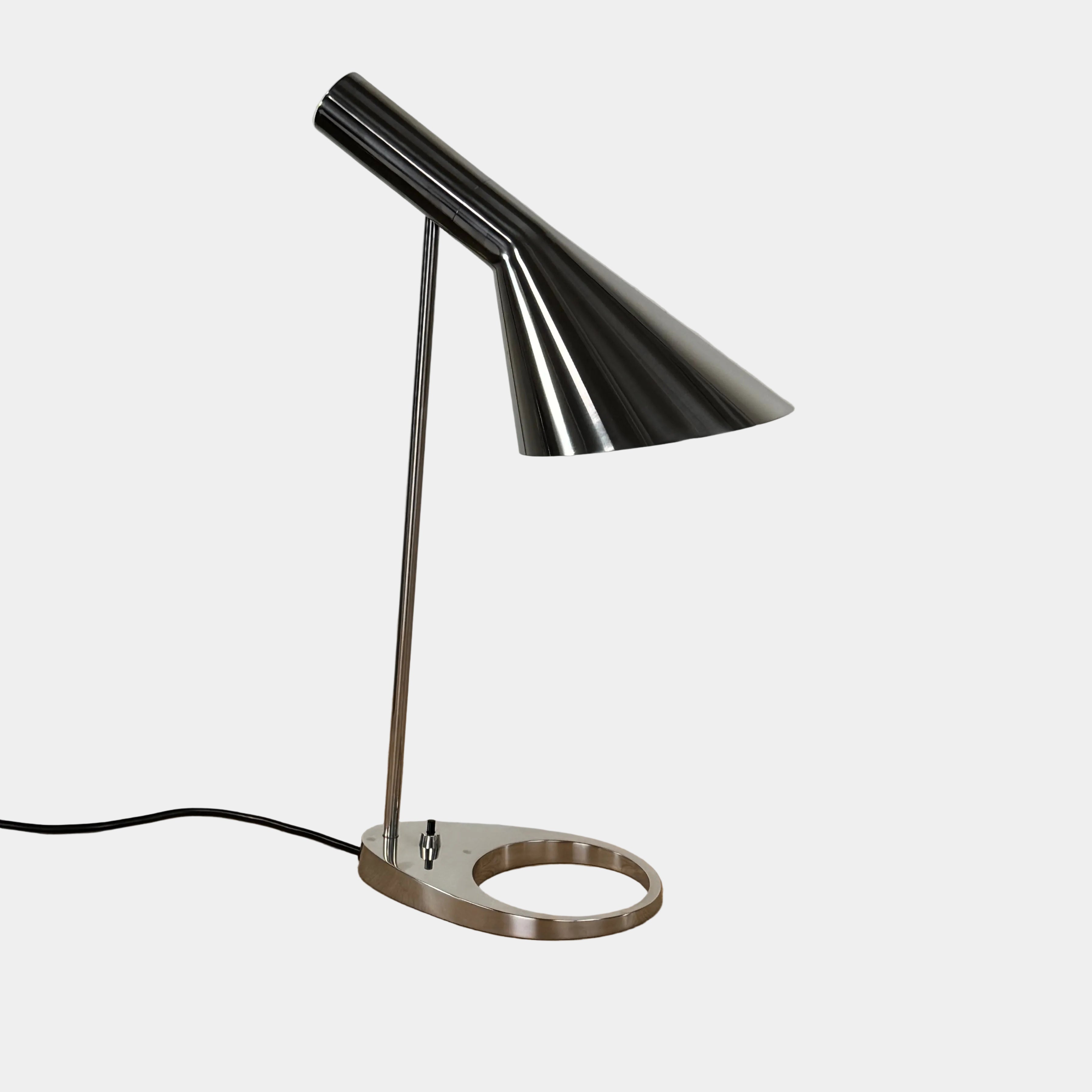 The Louis Poulsen AJ Table Lamp, featuring a modern metallic finish and slanted shade, rests on a wooden surface and illuminates the desk.