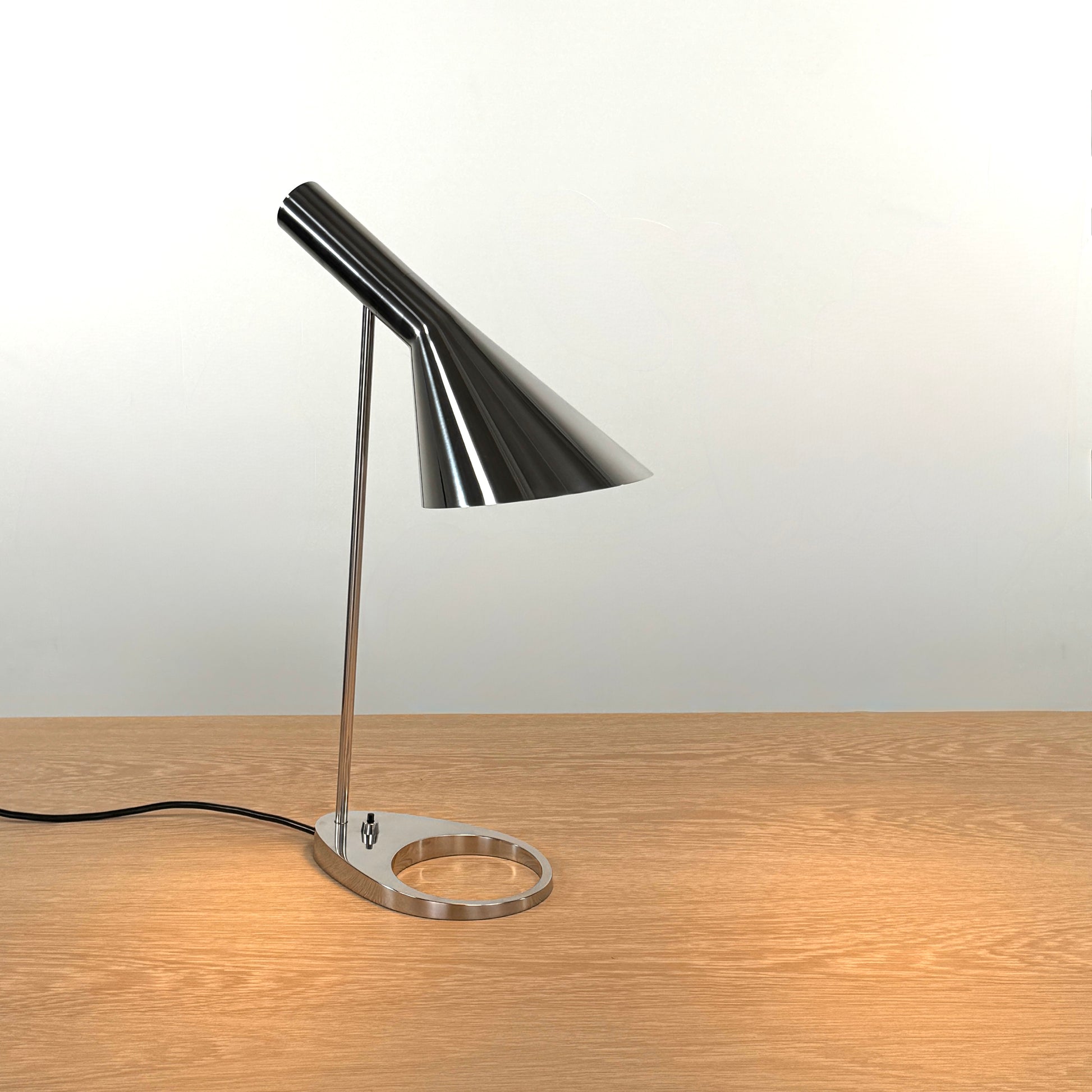The Louis Poulsen AJ Table Lamp, featuring a modern metallic finish and slanted shade, rests on a wooden surface and illuminates the desk.