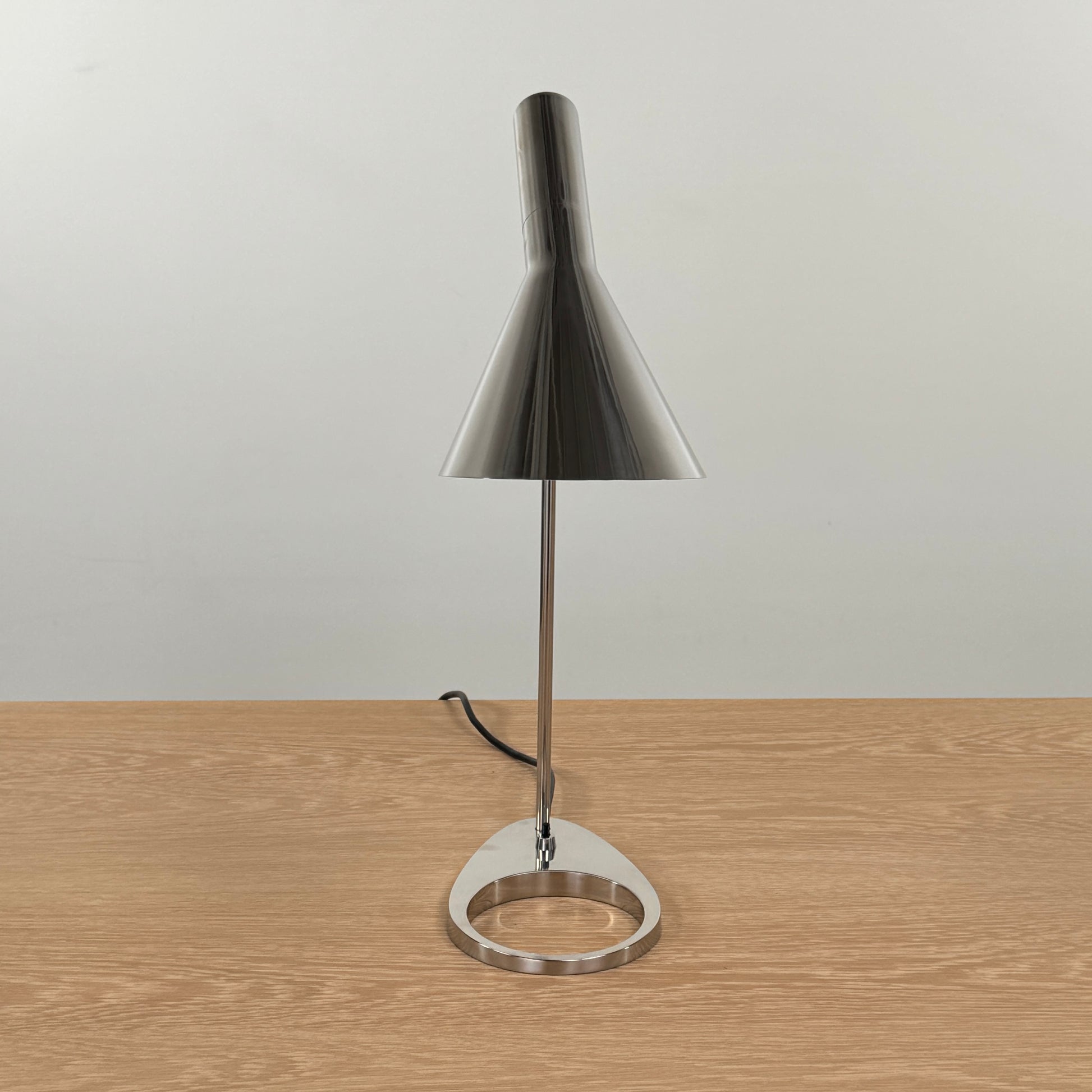 The Louis Poulsen AJ Table Lamp, featuring a modern metallic finish and slanted shade, rests on a wooden surface and illuminates the desk.