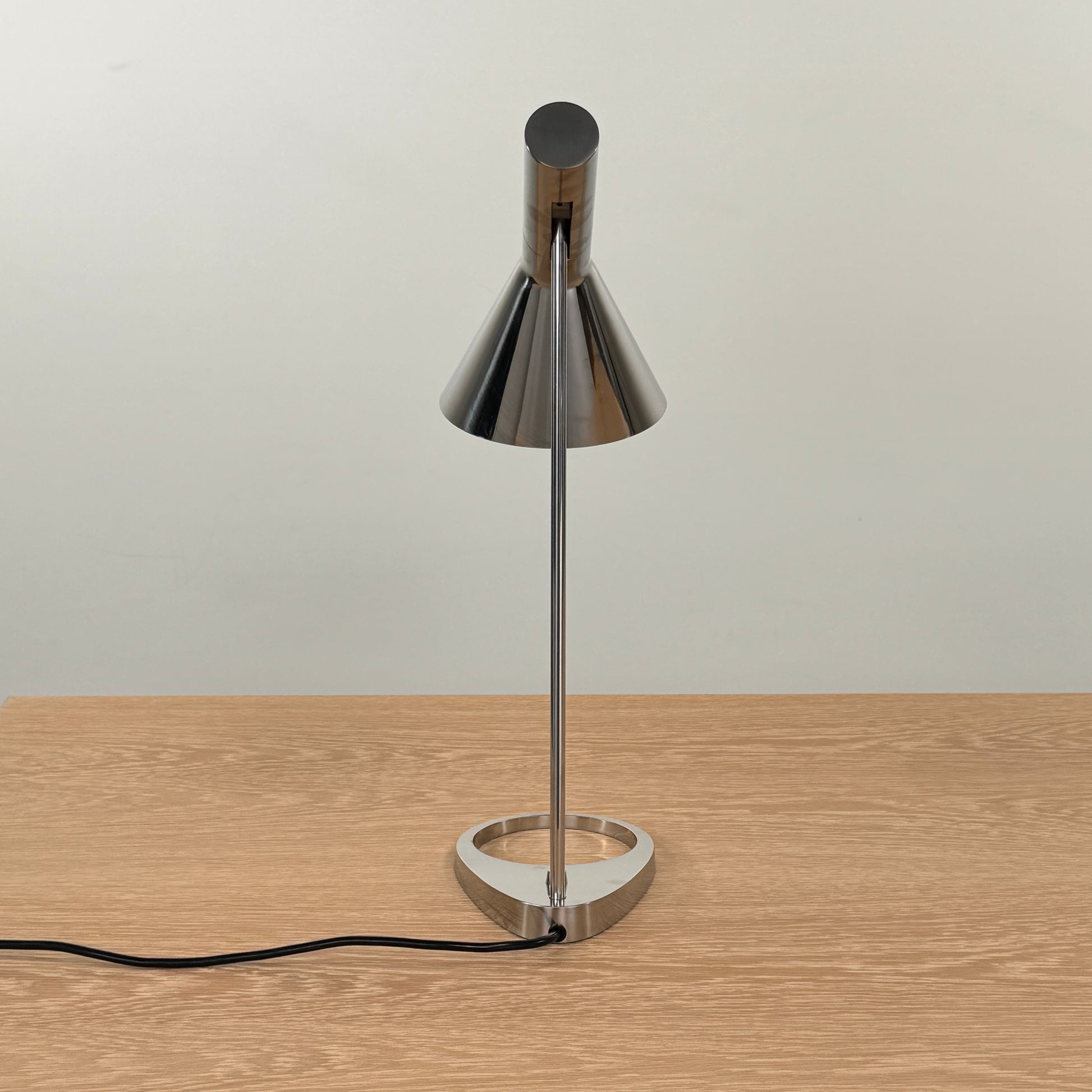 The Louis Poulsen AJ Table Lamp, featuring a modern metallic finish and slanted shade, rests on a wooden surface and illuminates the desk.