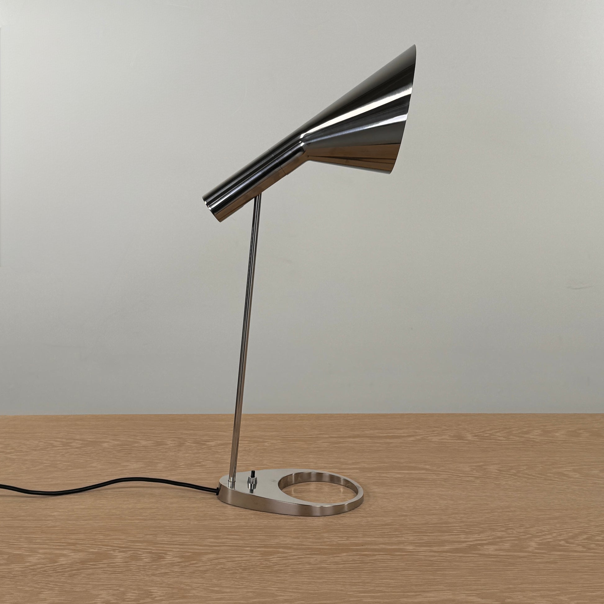The Louis Poulsen AJ Table Lamp, featuring a modern metallic finish and slanted shade, rests on a wooden surface and illuminates the desk.