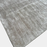 A close-up view of the Limited Edition 10 x 13.5′ Silk Rug, a rectangular, light gray area rug featuring a subtle textured pattern, crafted by the renowned Belgian brand Limited Edition. The luxurious silk rug is photographed against a plain white background.