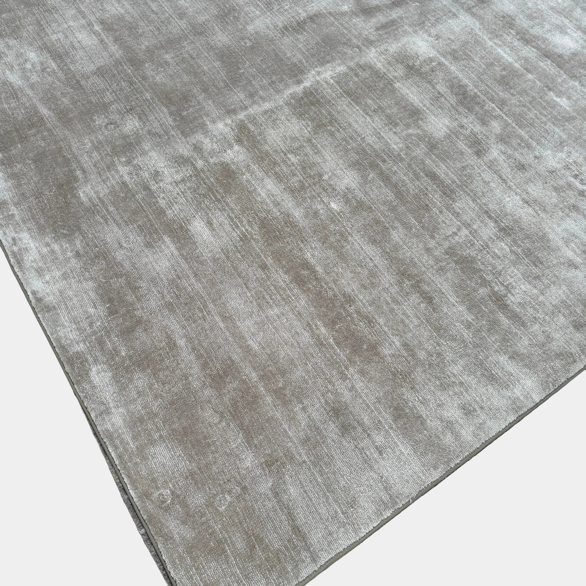 A close-up view of the Limited Edition 10 x 13.5′ Silk Rug, a rectangular, light gray area rug featuring a subtle textured pattern, crafted by the renowned Belgian brand Limited Edition. The luxurious silk rug is photographed against a plain white background.