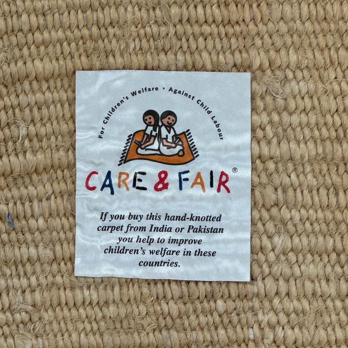 A rectangular Nanimarquina Tres Rug in Ocher, showcasing a patchwork design in warm beige and brown hues, is displayed on a concrete floor. This artisanal piece by Nanimarquina features hand-woven techniques and decorative fringe along two opposite edges, reminiscent of the brand’s signature style.